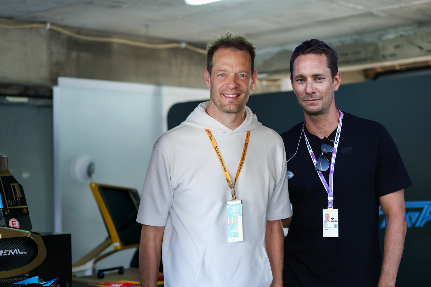 Alexander Wurz im weißen Kapuzenpullover und Mathias Lauda im schwarzen T-Shirt lächeln nebeneinander in die Kamera.