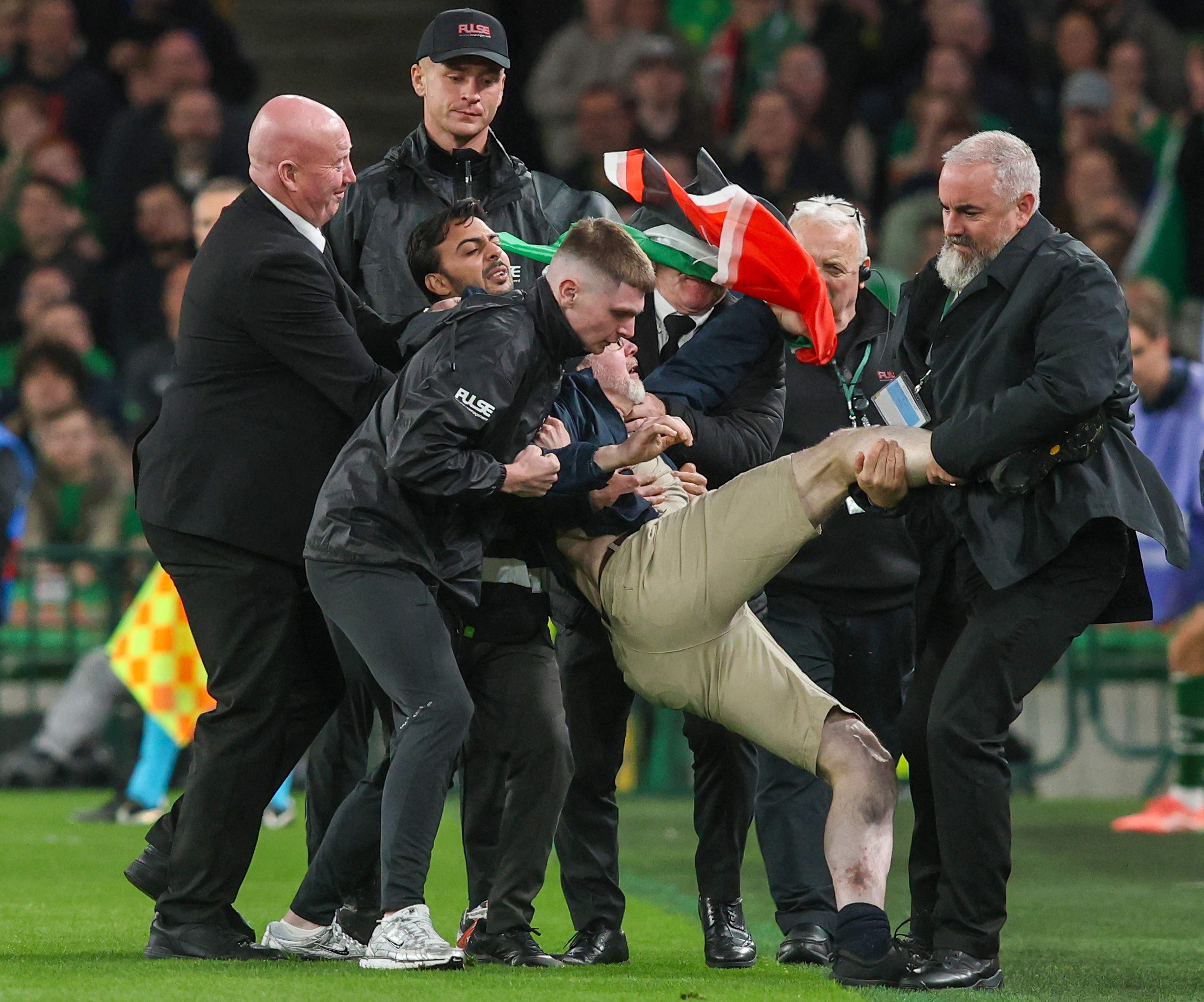 Sicherheitskräfte entfernen einen Flitzer während eines Fußballspiels vom Spielfeld.