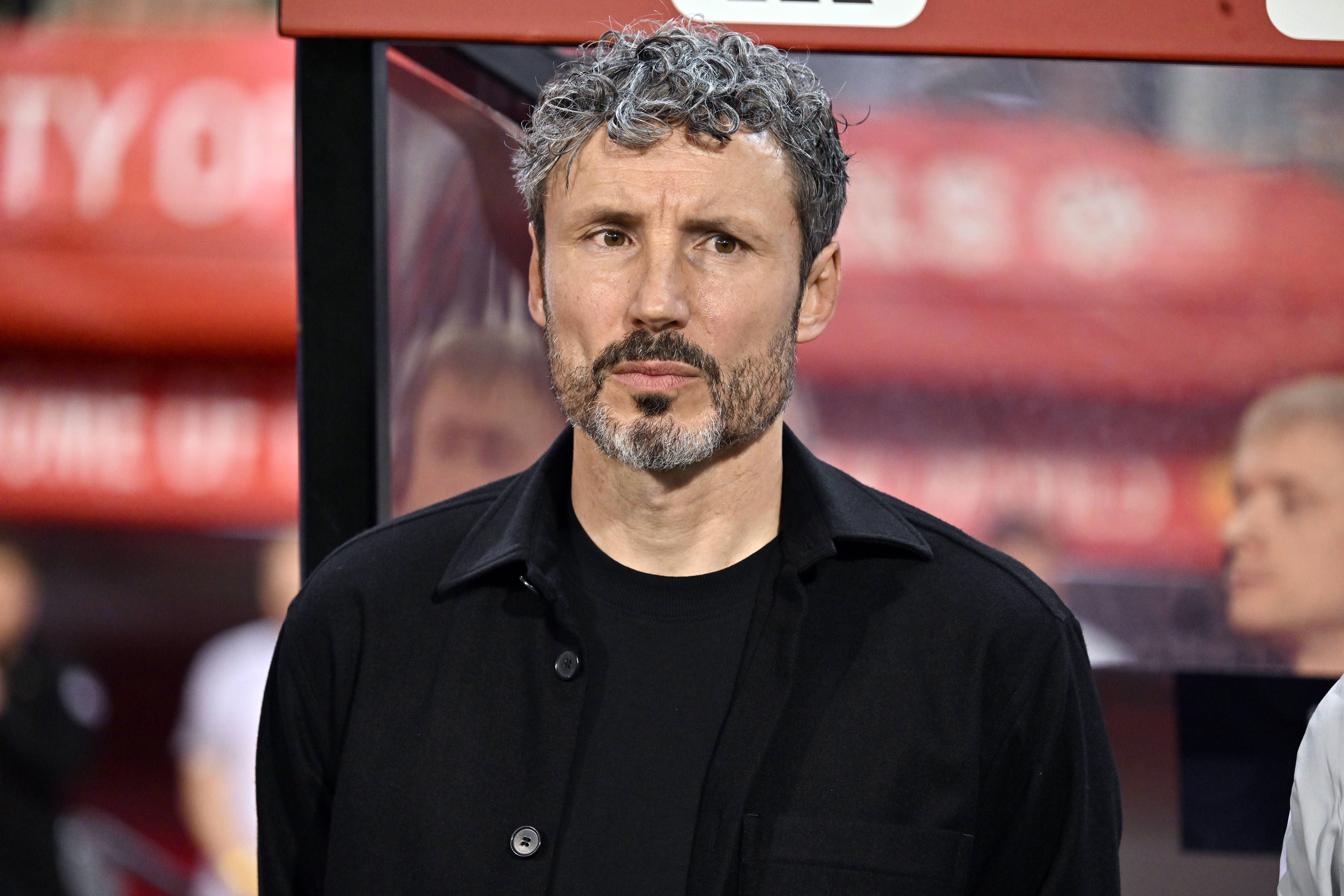 Mark van Bommel blickt mit ernster Miene und verschränkten Armen an der Trainerbank nach vorne.