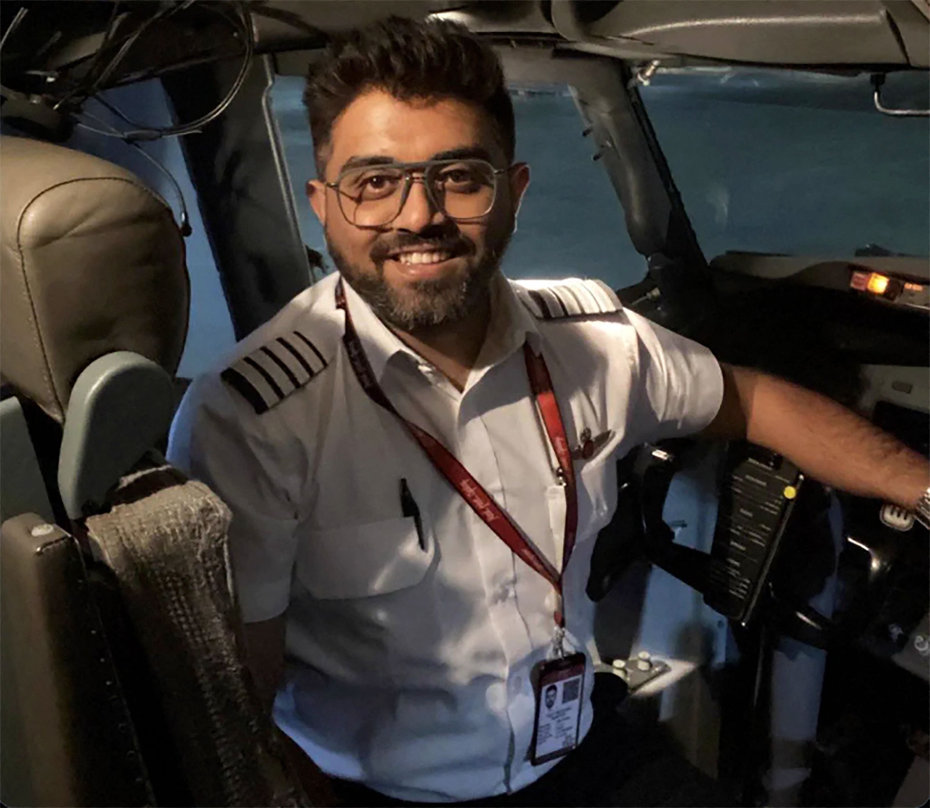 Ein Pilot mit Brille und Uniform sitzt lächelnd im Cockpit eines Flugzeugs.