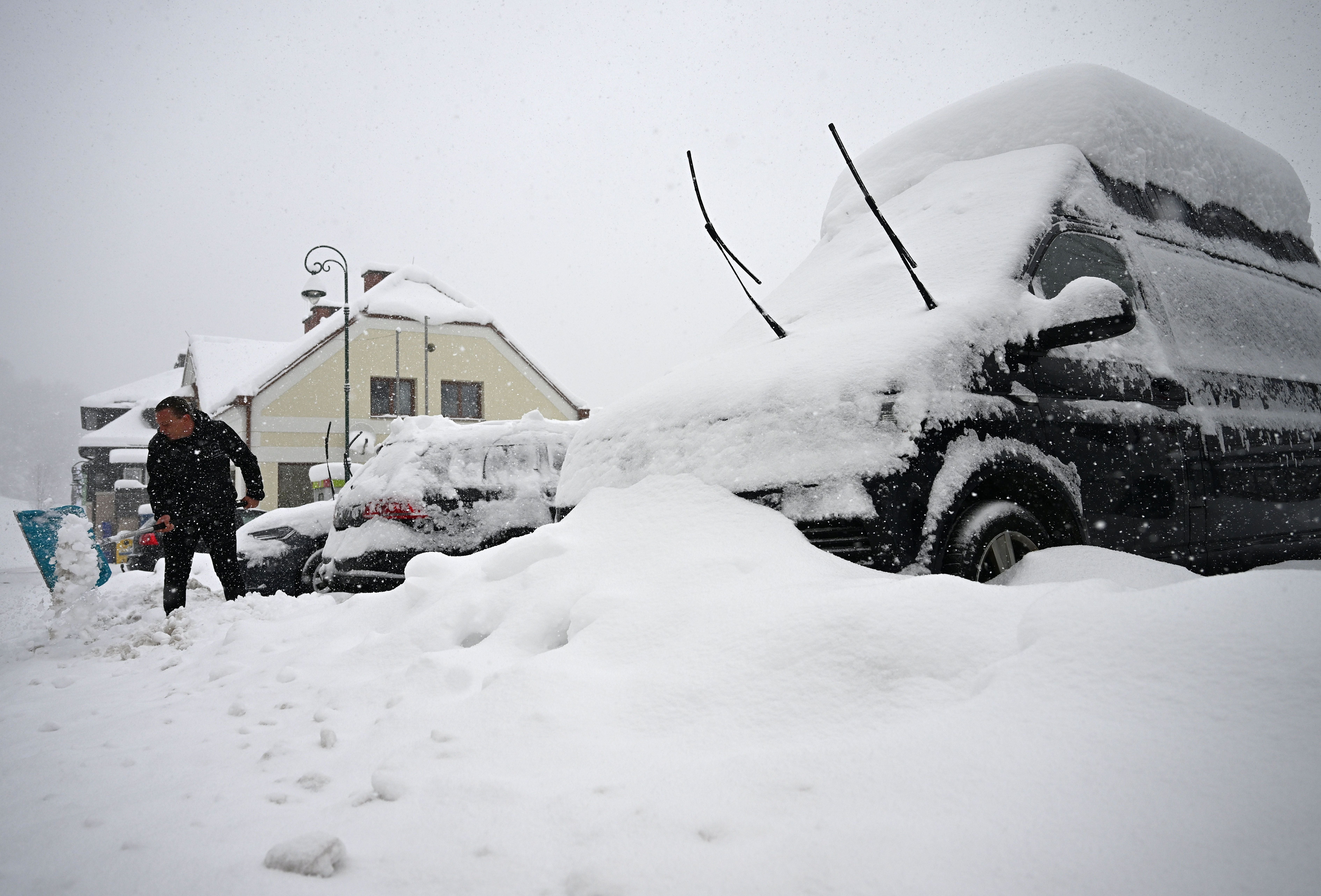 Ein Mann räumt Schnee neben verschneiten Autos vor einem Haus in Puchenstuben, Österreich.