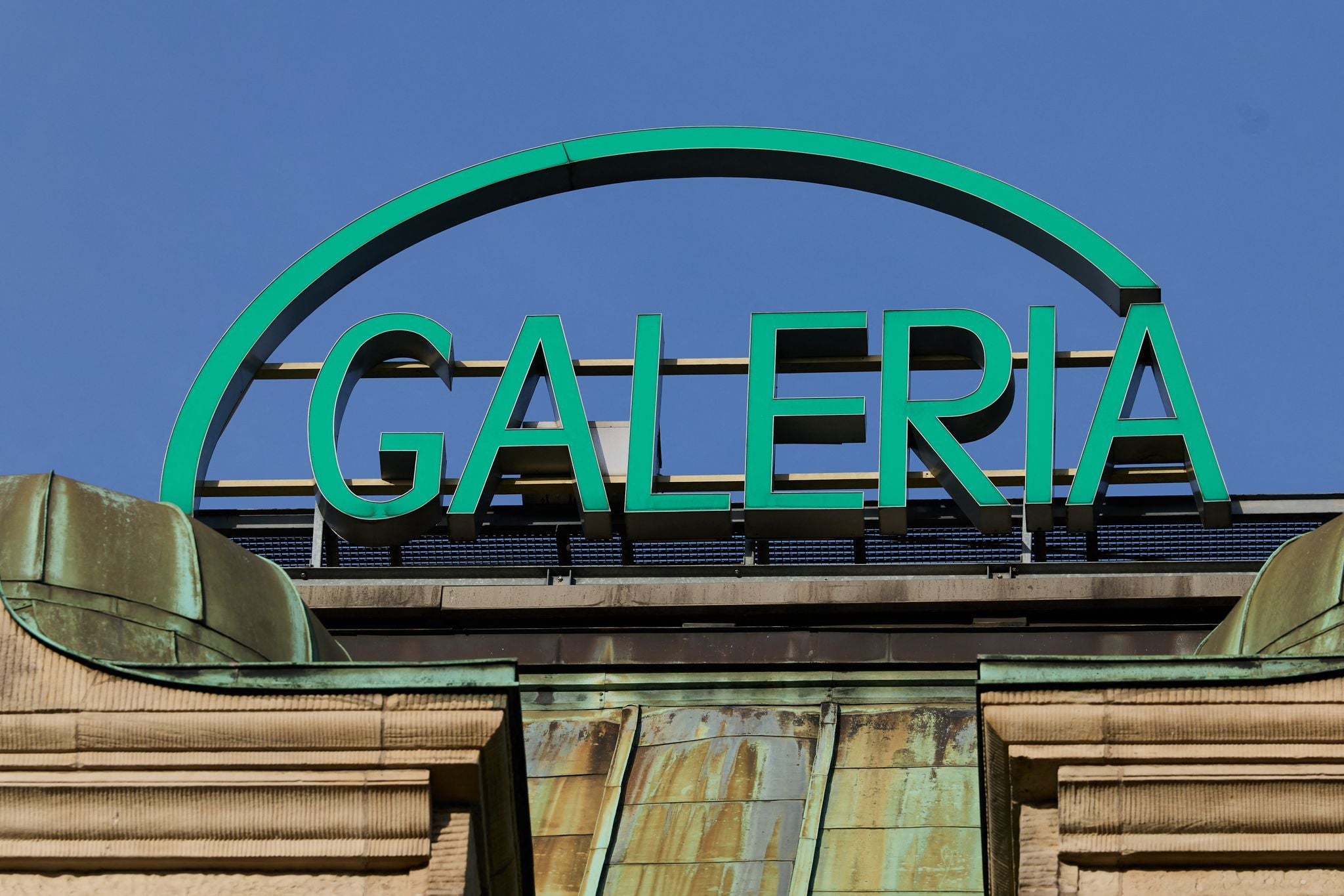 Grünes "Galeria"-Schild auf einem Dach mit blauem Himmel im Hintergrund.