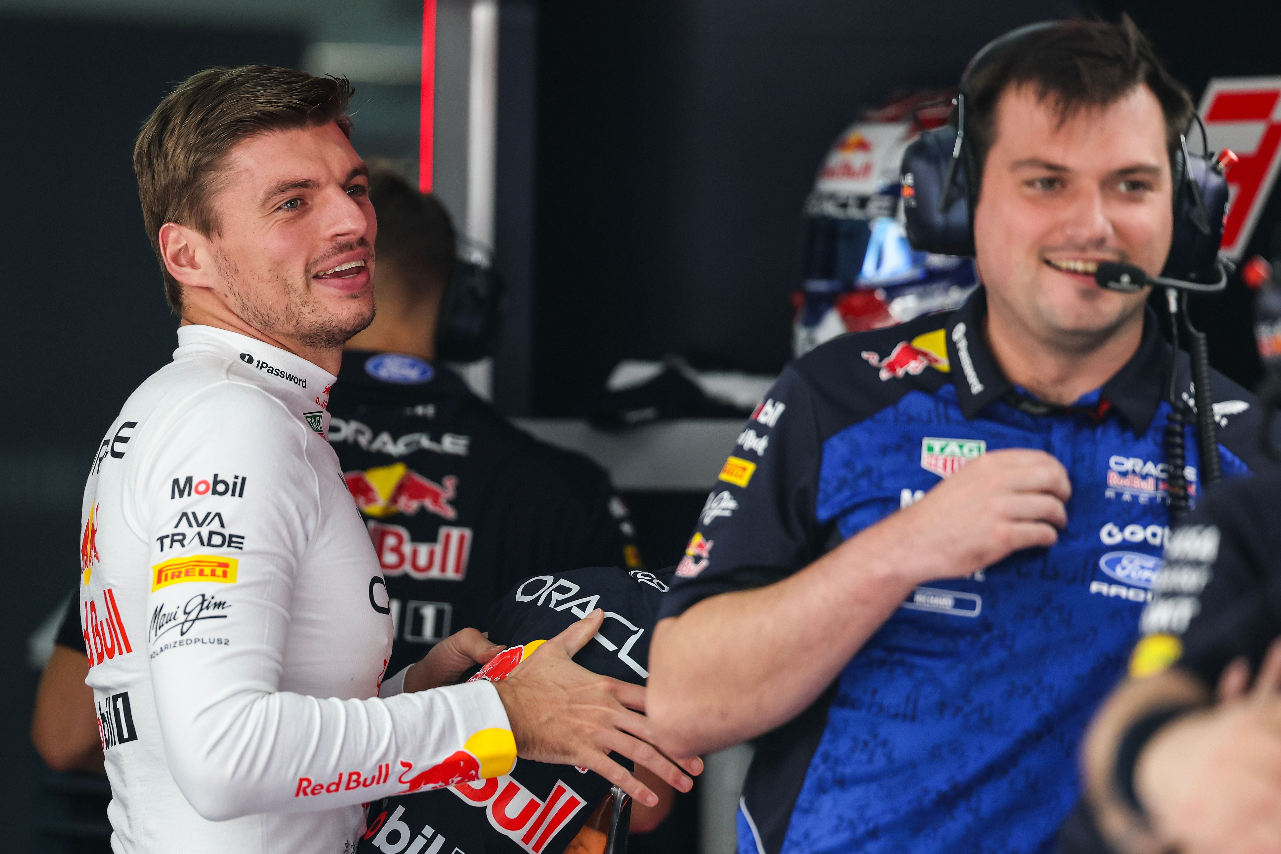 Zwei Männer im Red-Bull-Teamoutfit lächeln in einer Formel-1-Boxengasse.