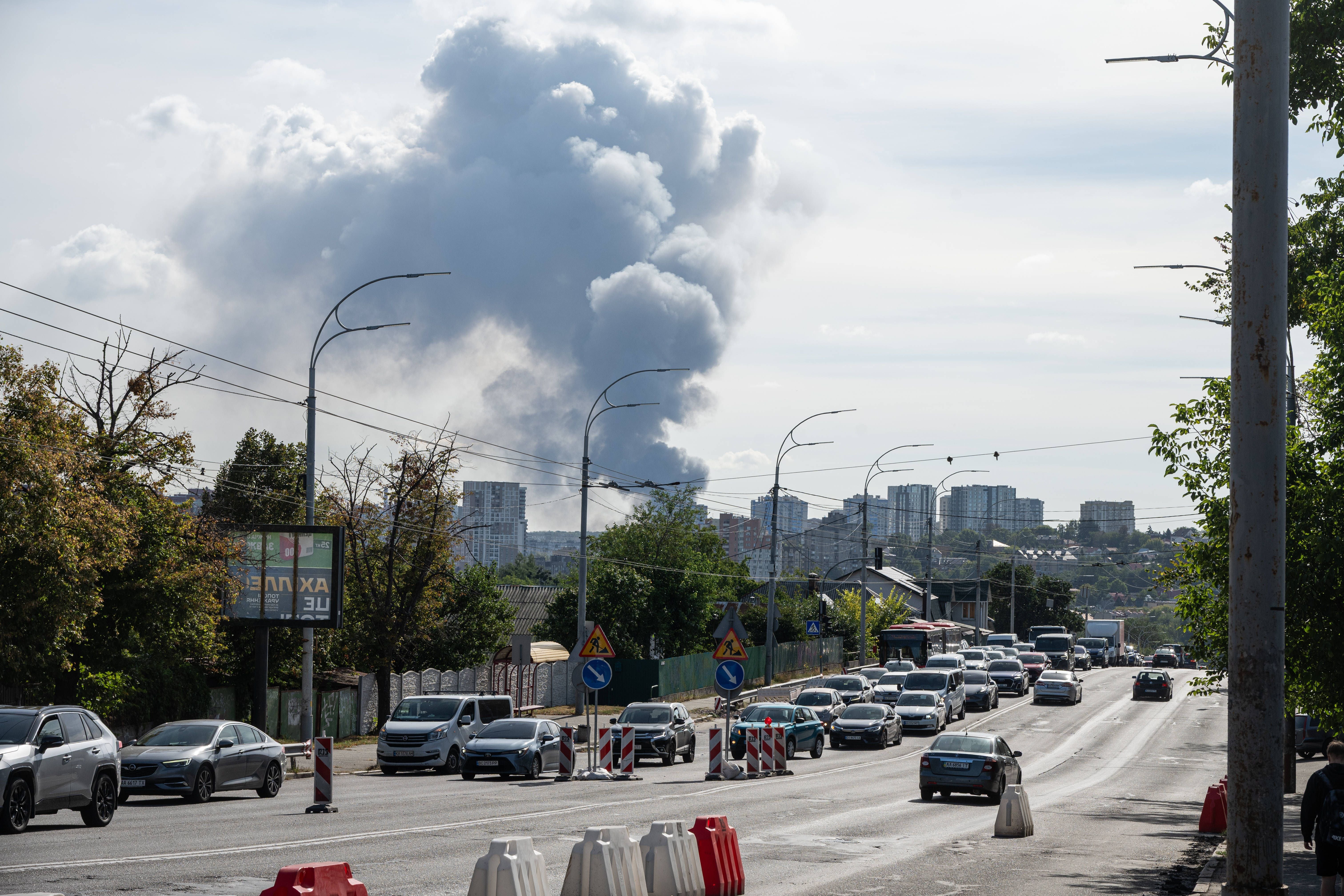 Rauchwolke steigt nach russischem Luftangriff über der Skyline von Kiew auf, Autos auf Straße im Vordergrund.