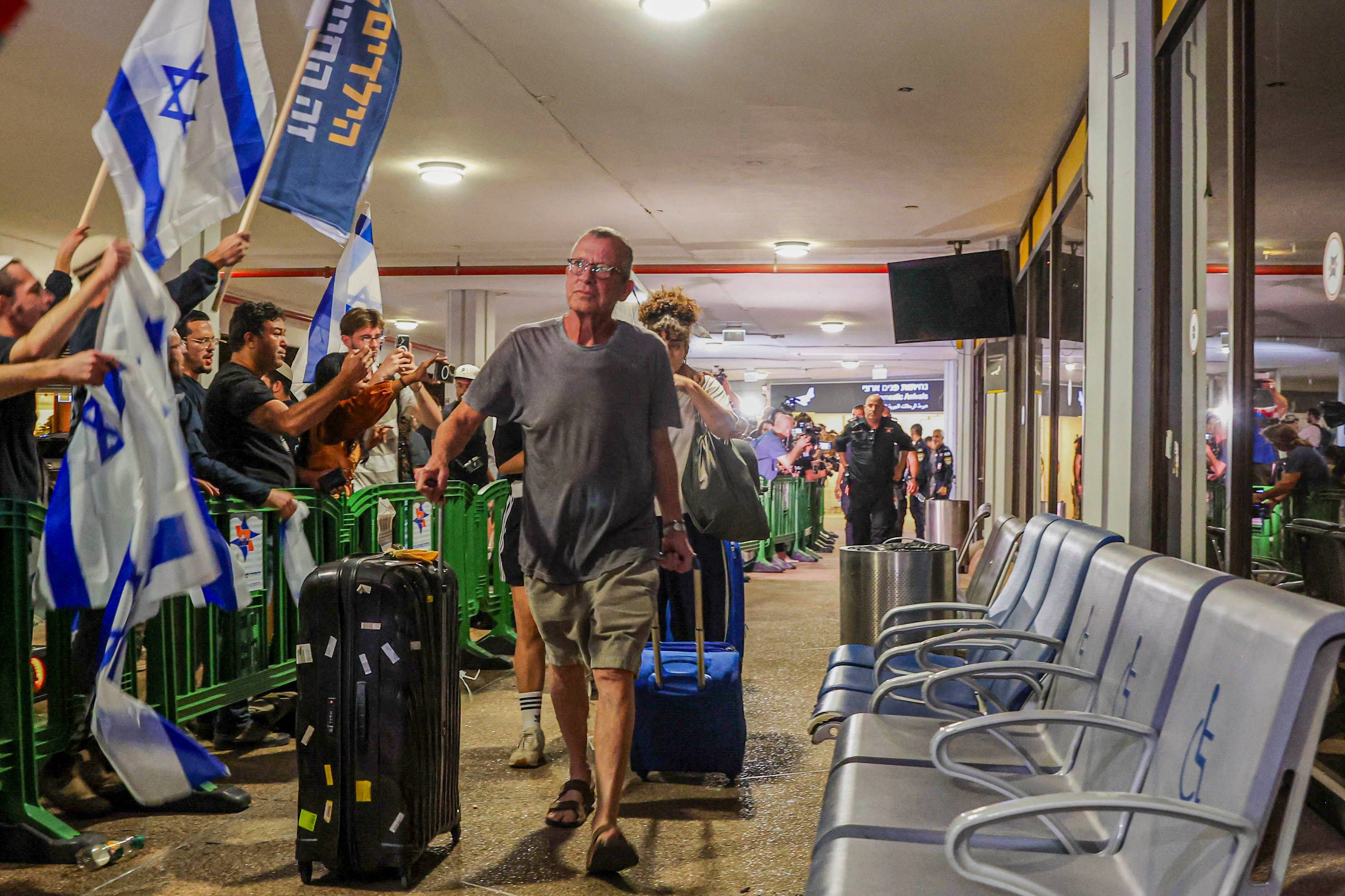 Passagiere mit Gepäck werden am Flughafen Tel Aviv von Menschen mit israelischen Fahnen begrüßt.