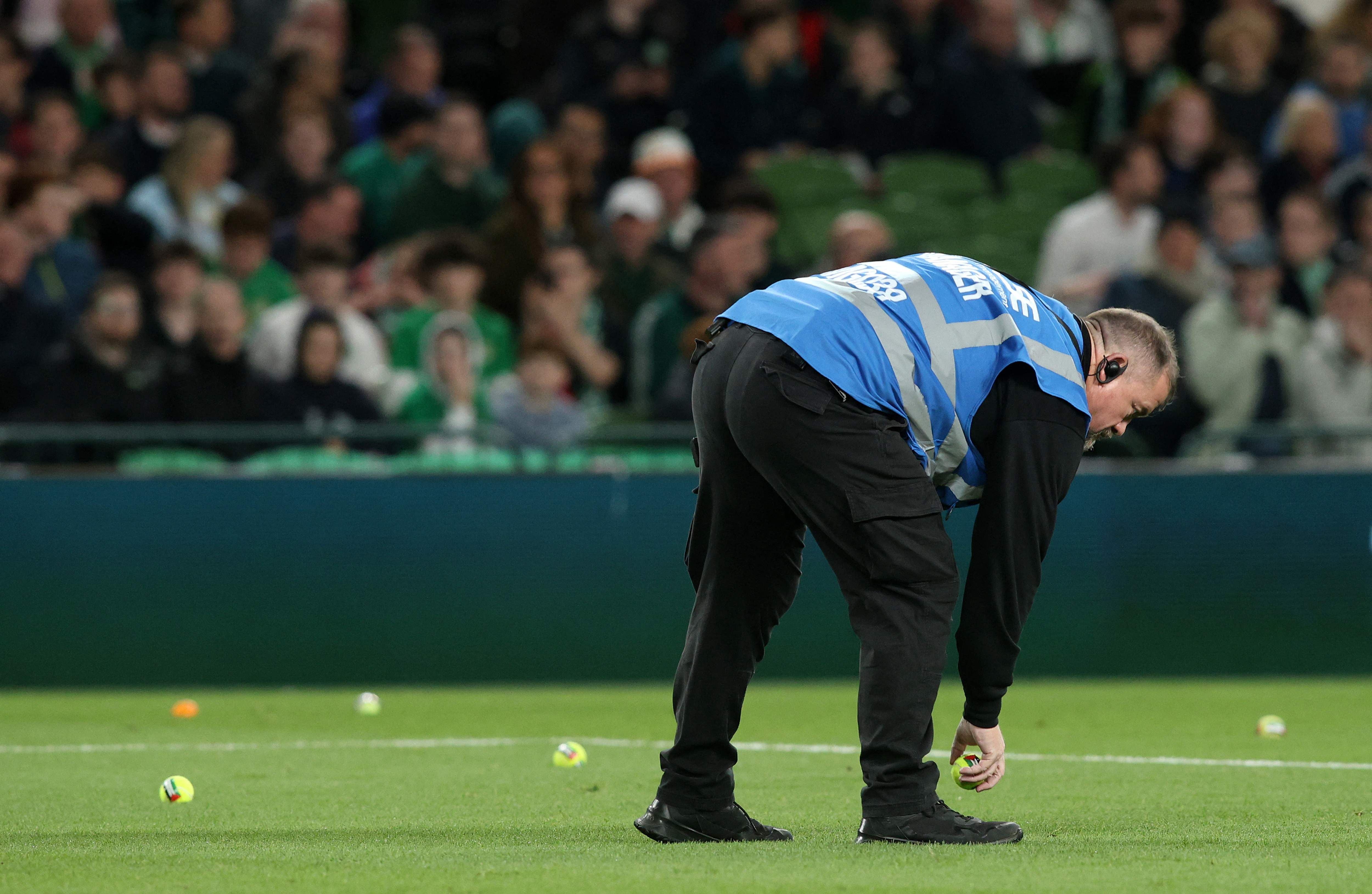 Ein Ordner sammelt auf das Spielfeld geworfene Tennisbälle während eines Fußballspiels ein.