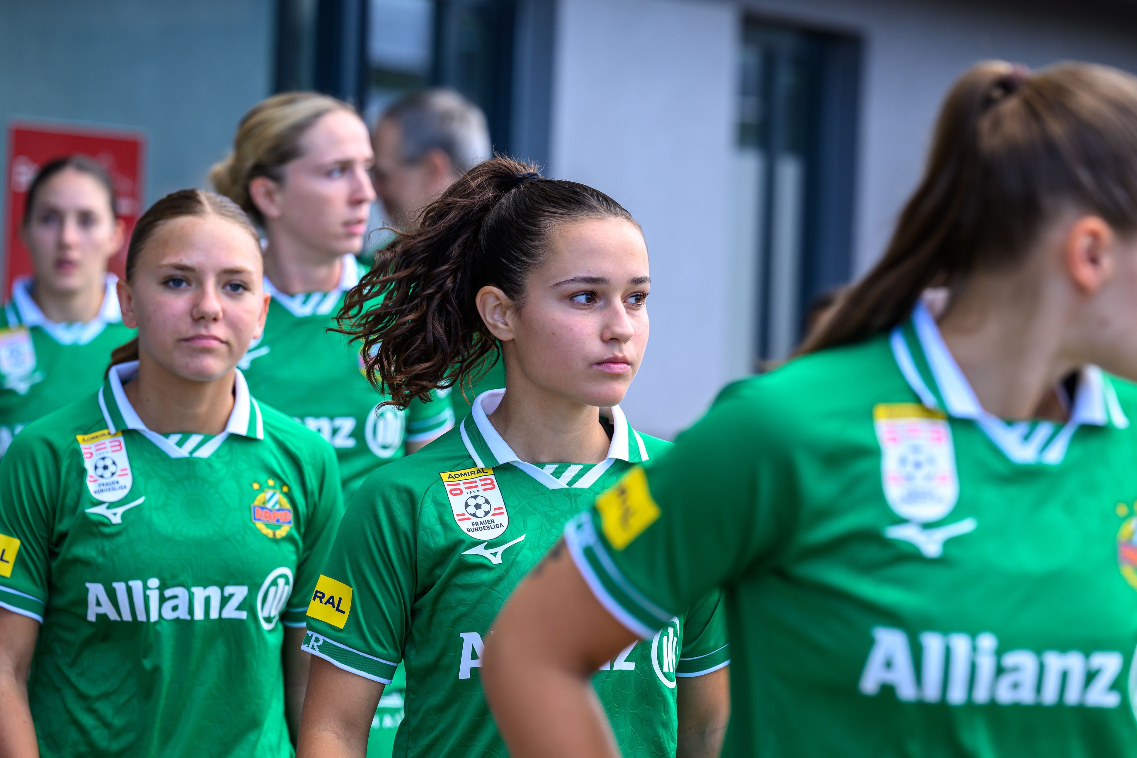 Mehrere Fußballspielerinnen im grünen Trikot von SK Rapid stehen nebeneinander auf dem Spielfeld.