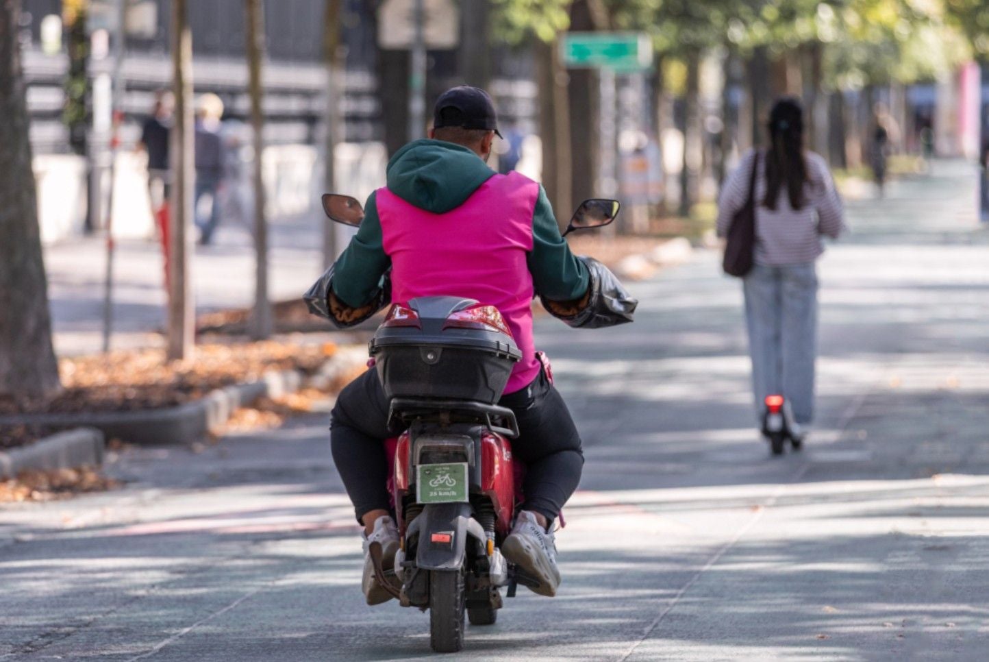 Person fährt auf einem E-Moped mit pinker Weste durch die Linzer Innenstadt.