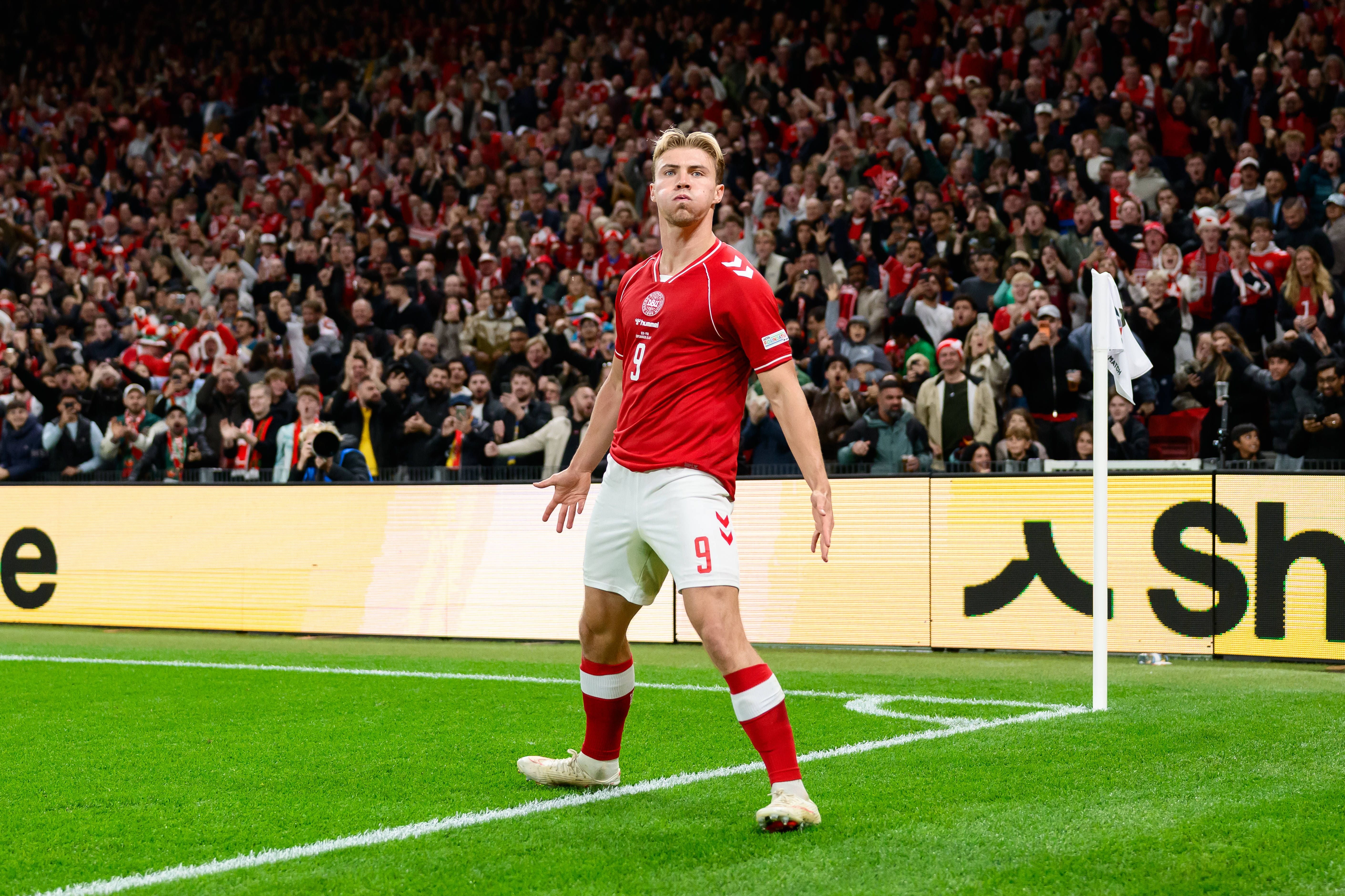 Dänischer Fußballspieler im roten Trikot jubelt nach einem Tor vor begeisterten Fans im Stadion.