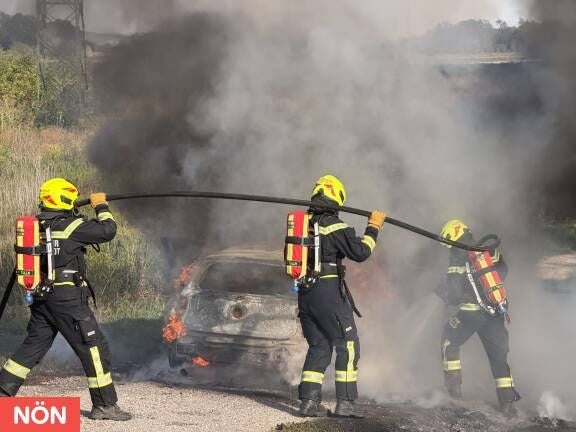 Drei Feuerwehrleute löschen ein brennendes Auto mit viel Rauch in Tulln.