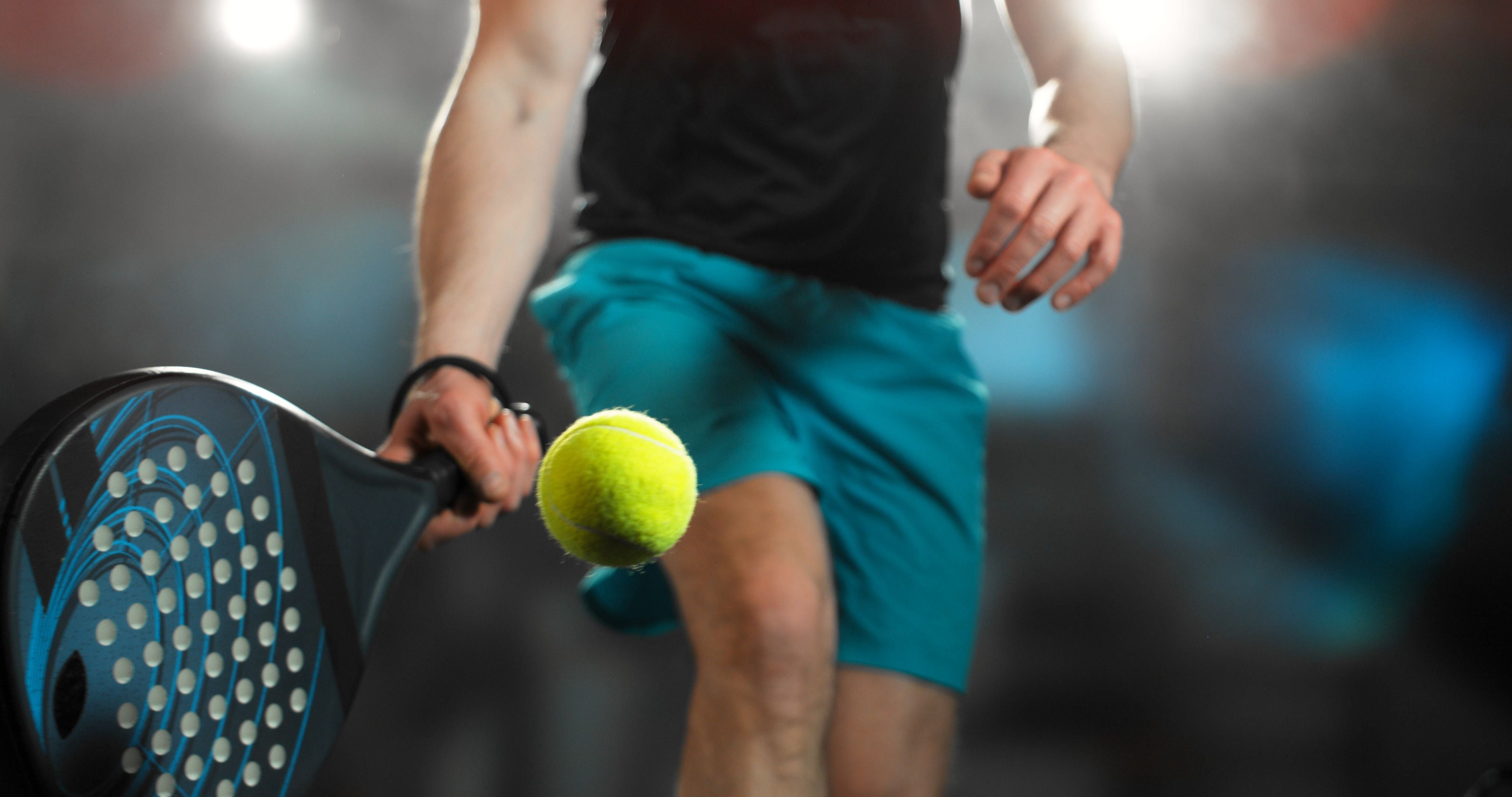 Padelspieler schlägt einen gelben Ball mit Schläger, dynamische Beleuchtung betont die Bewegung.