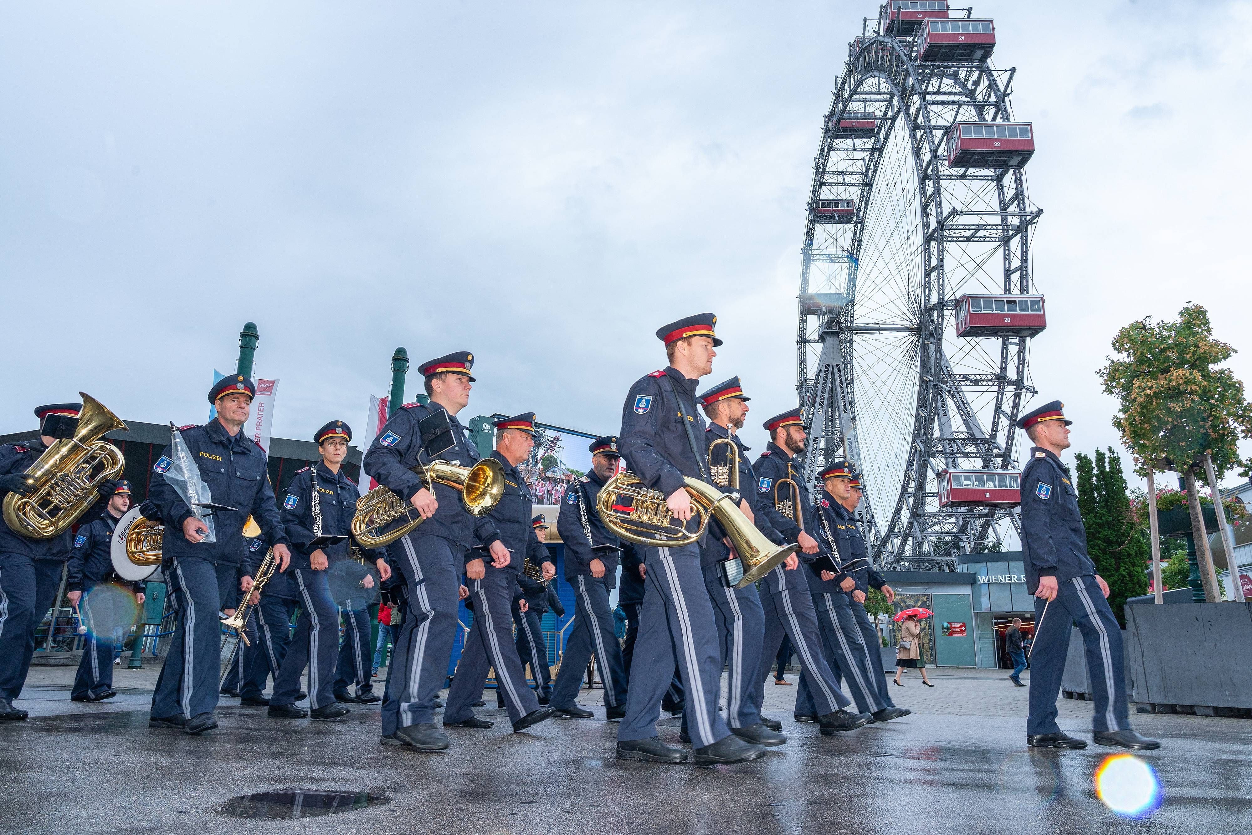 Eine Polizei-Musikkapelle marschiert mit Instrumenten vor dem Wiener Riesenrad im Prater.