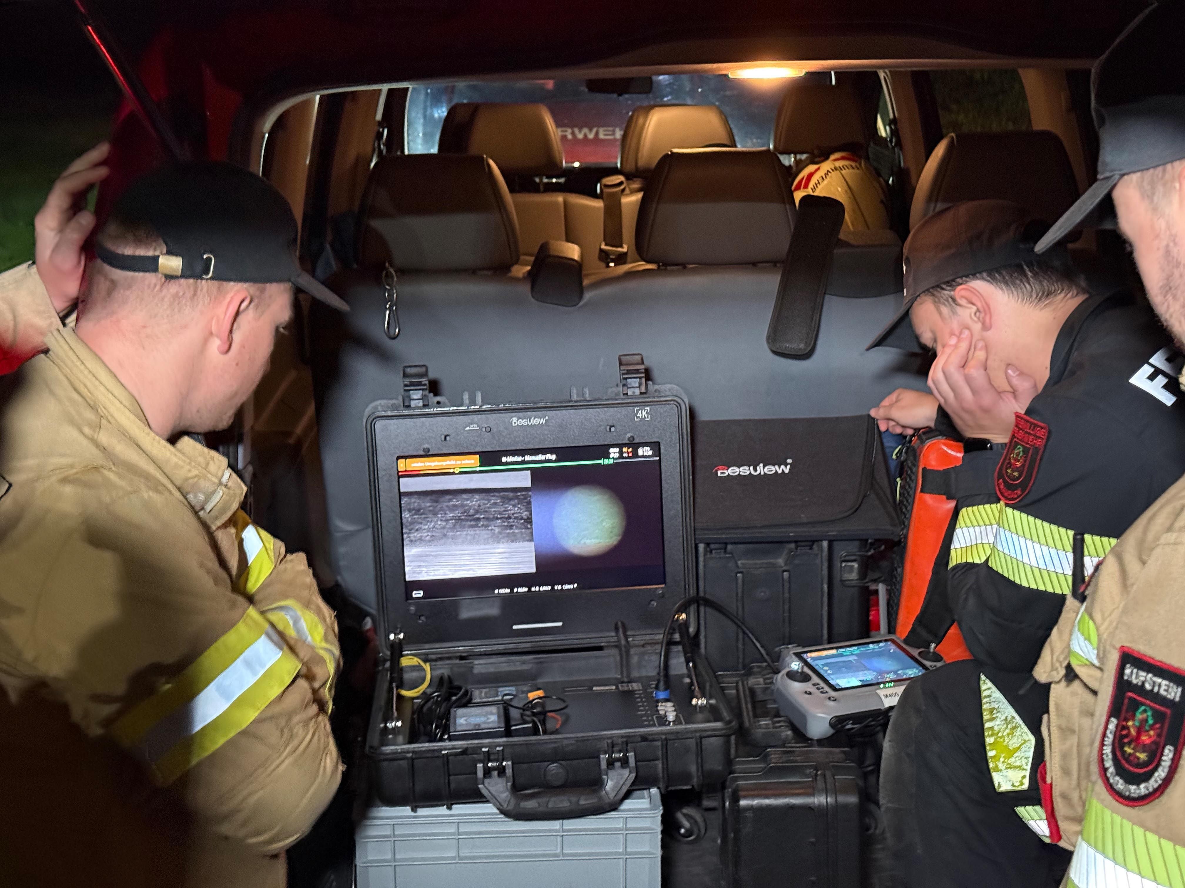 Drei Feuerwehrleute überwachen eine Kameraaufnahme auf einem Monitor im Auto.