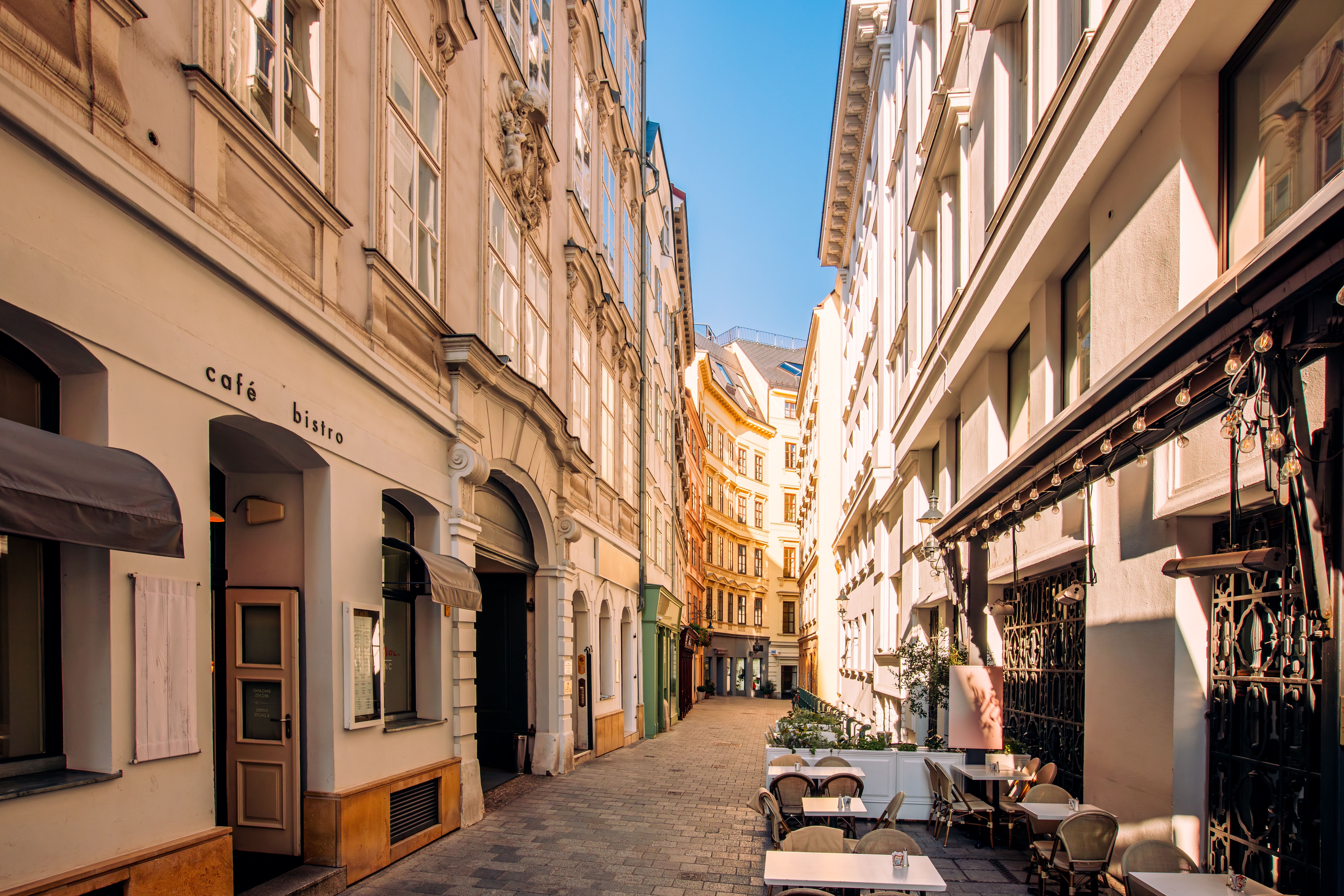 Schmale Gasse in Wien mit Straßencafés und historischen Gebäuden bei sonnigem Wetter.