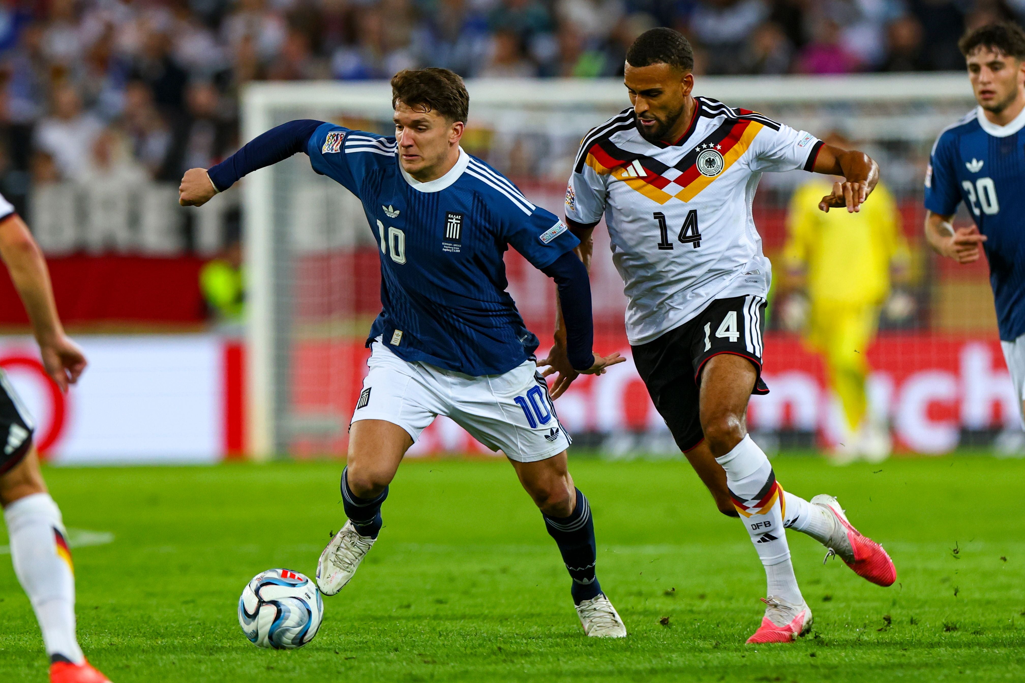 Christos Tzolis im blauen Trikot von Griechenland behauptet den Ball im Zweikampf gegen Jonathan Tah im weißen DFB-Trikot.