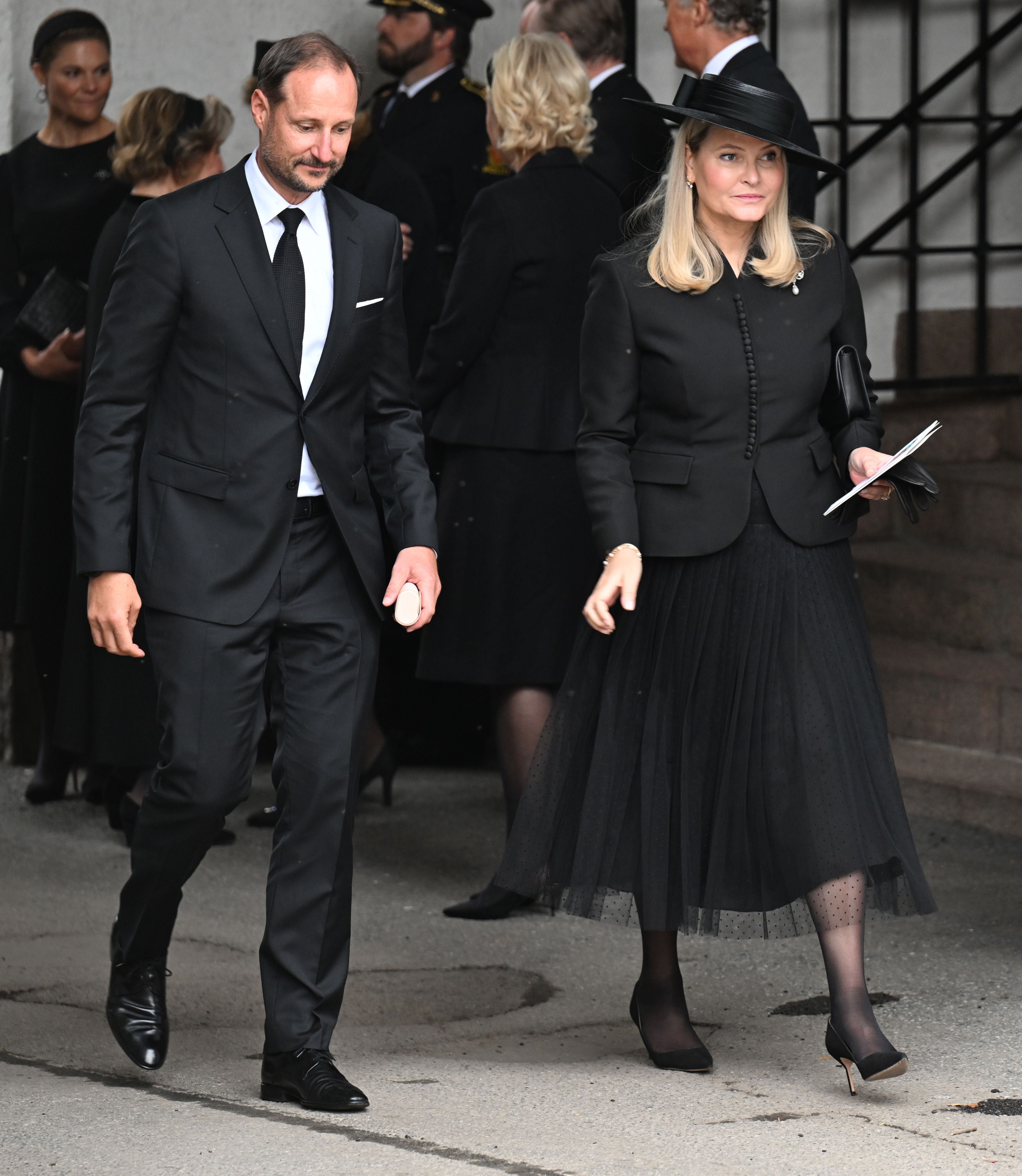 Ein Mann und eine Frau in formeller schwarzer Kleidung gehen bei einer Trauerfeier.
