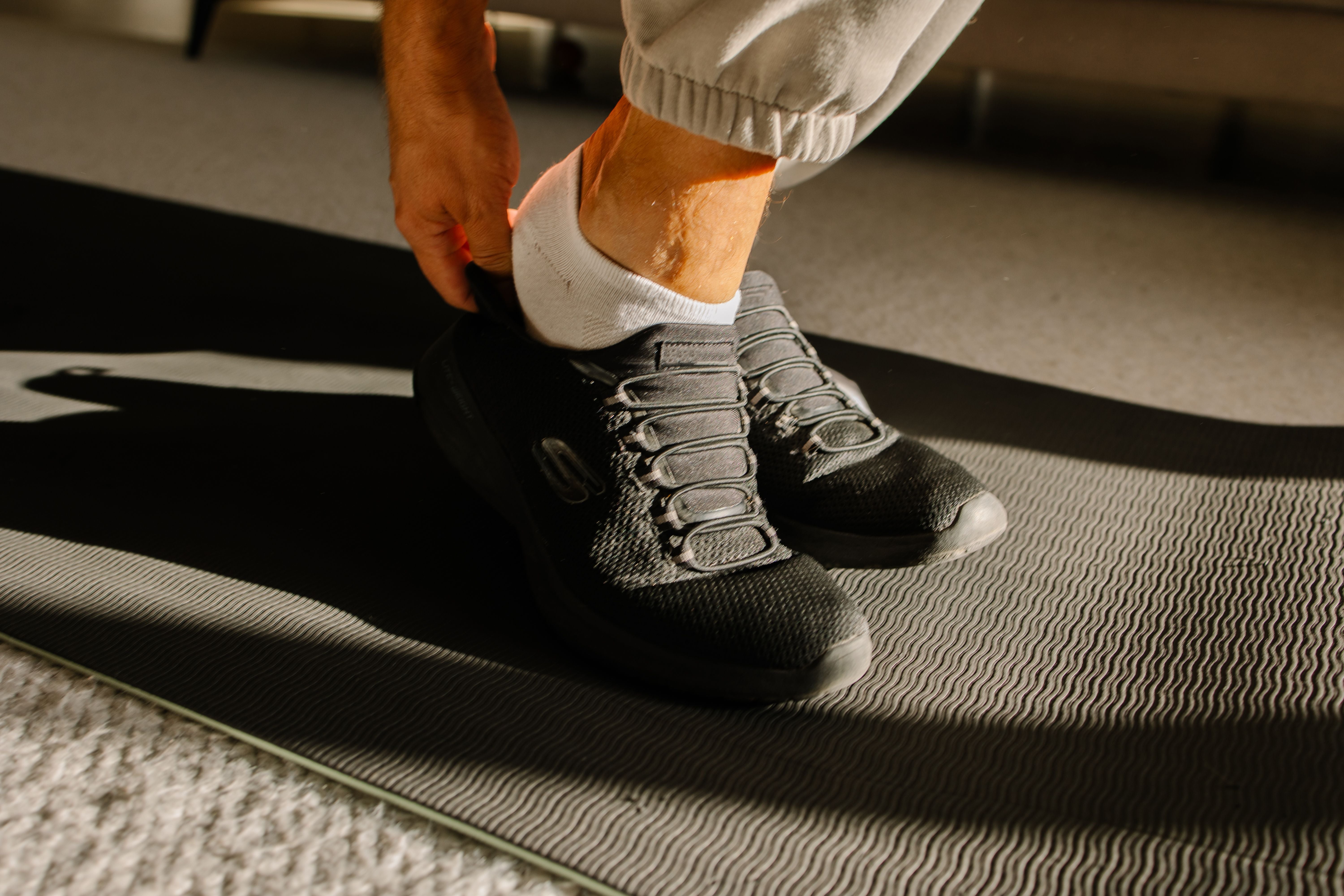 Mann zieht Sportschuhe auf einer Fitnessmatte an, bereit für das Training zu Hause.
