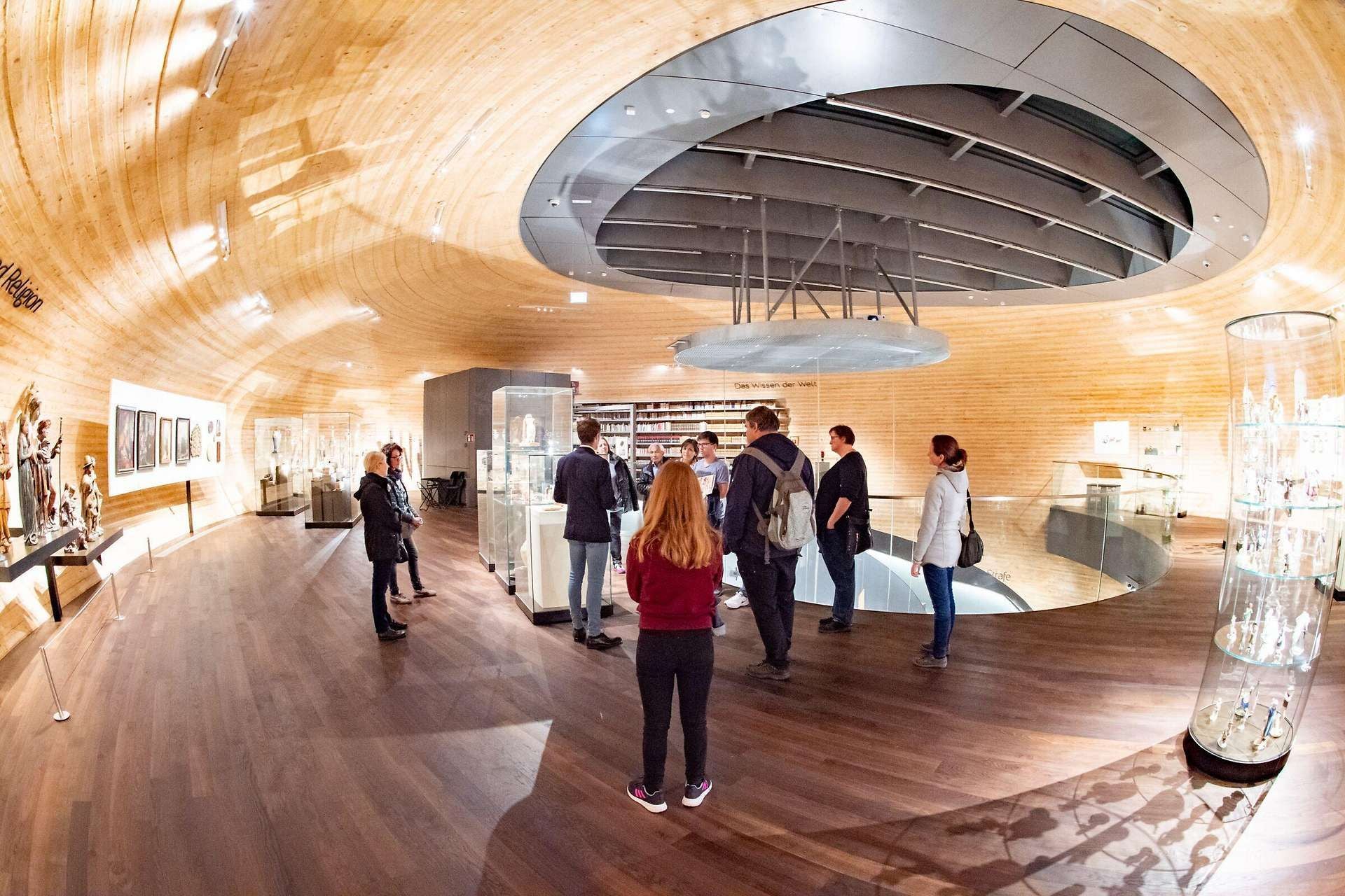 Gruppe von Menschen in einem modernen, hellen Museumsraum mit Holzdecke und Vitrinen.