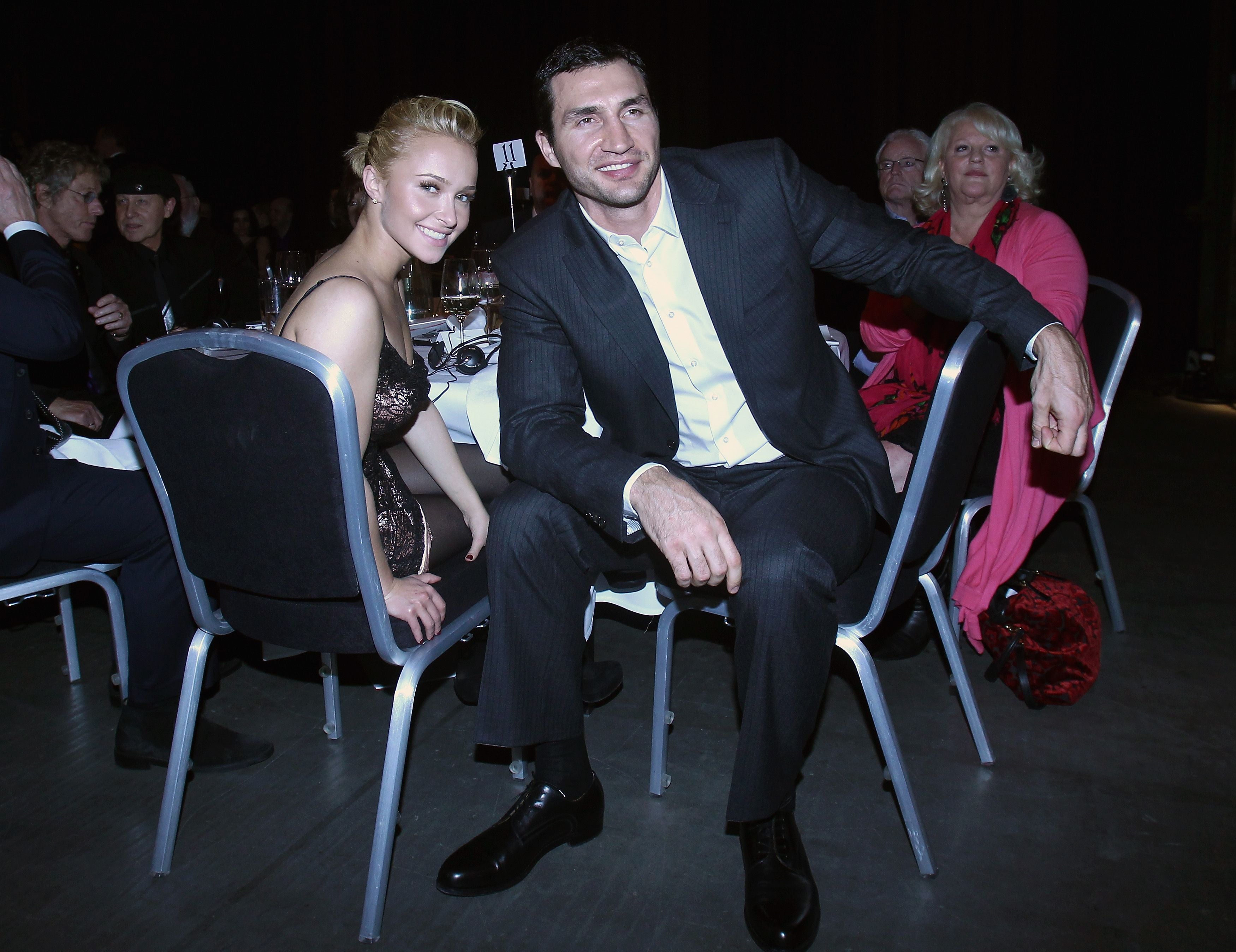 Ein lächelndes Paar sitzt elegant gekleidet an einem Tisch bei einer Gala-Veranstaltung.