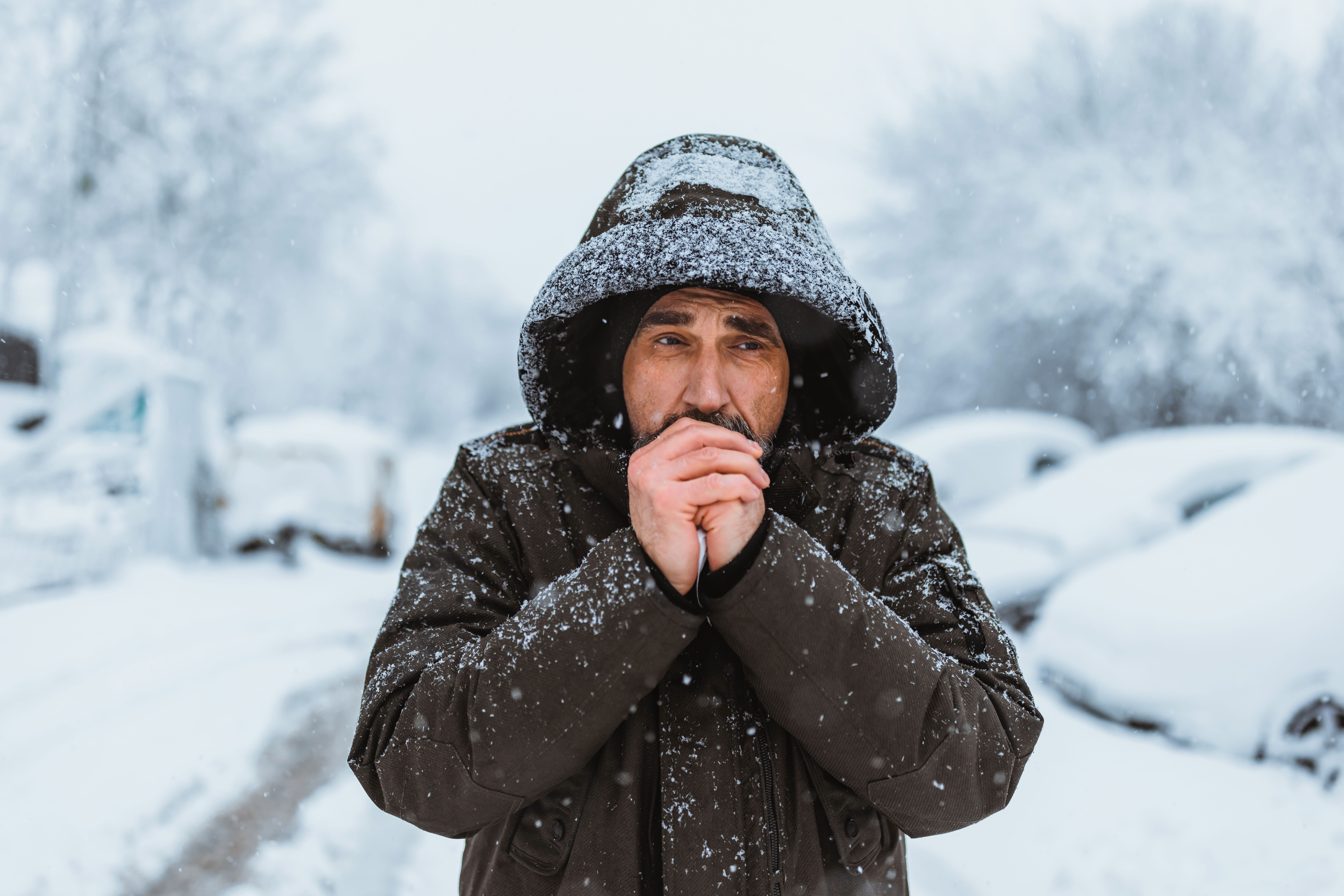 Mann mit Kapuze steht im Schnee und wärmt seine Hände im winterlichen Freien.
