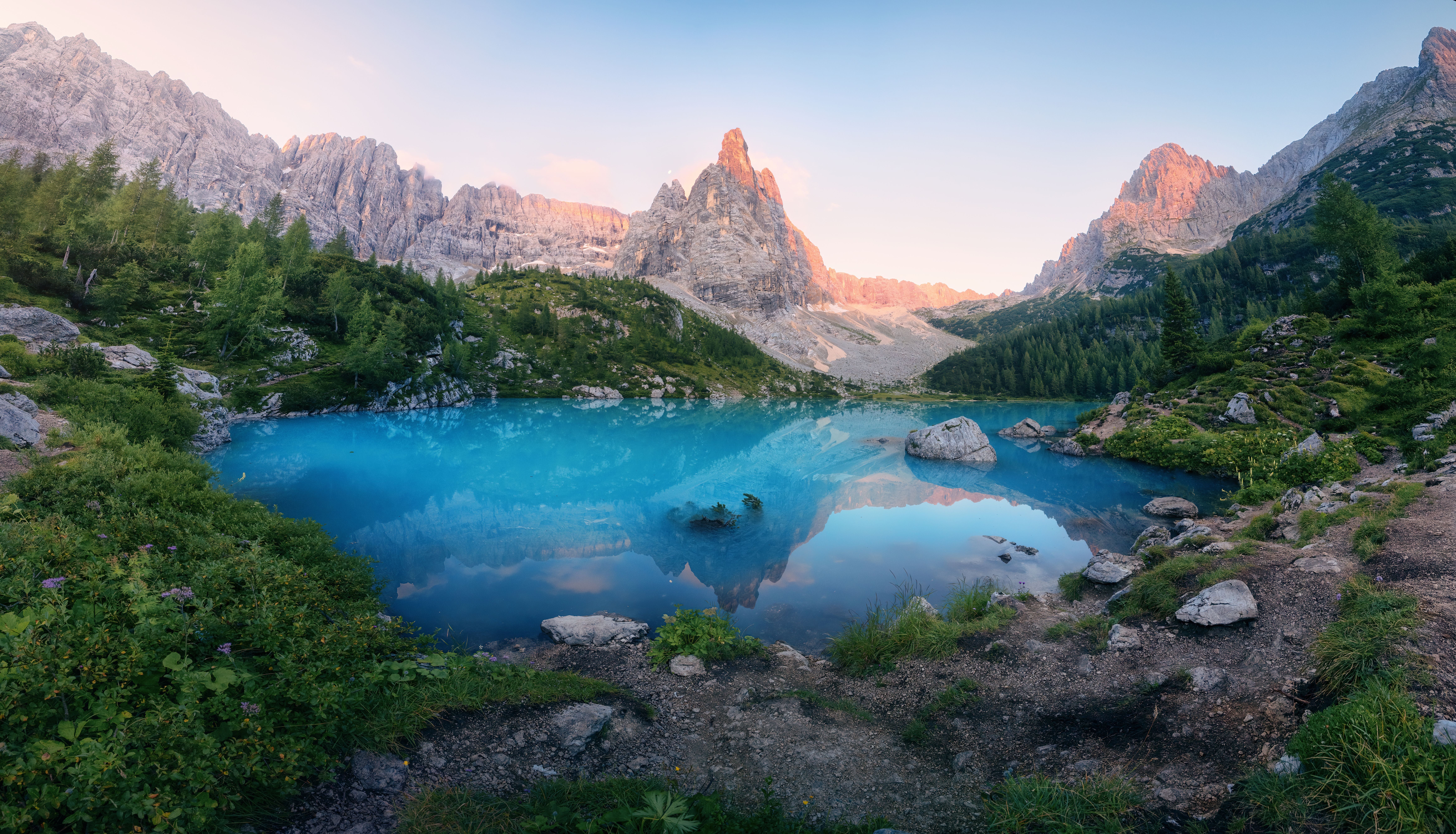 Panoramafoto eines türkisblauen Sees in den Dolomiten mit Bergen im Sonnenaufgang.