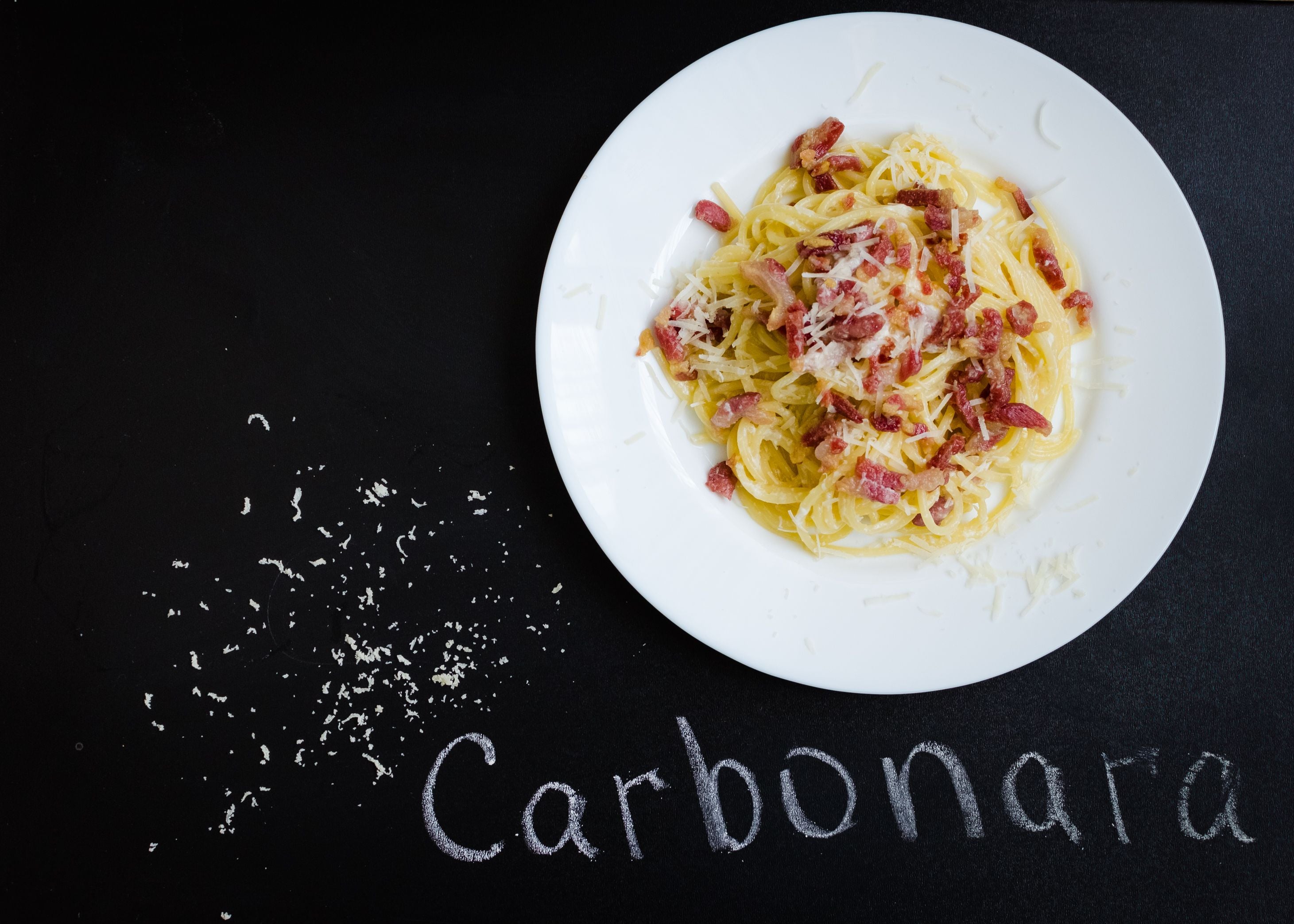Spaghetti Carbonara mit Speck und Parmesan auf weißem Teller, daneben das Wort "Carbonara".