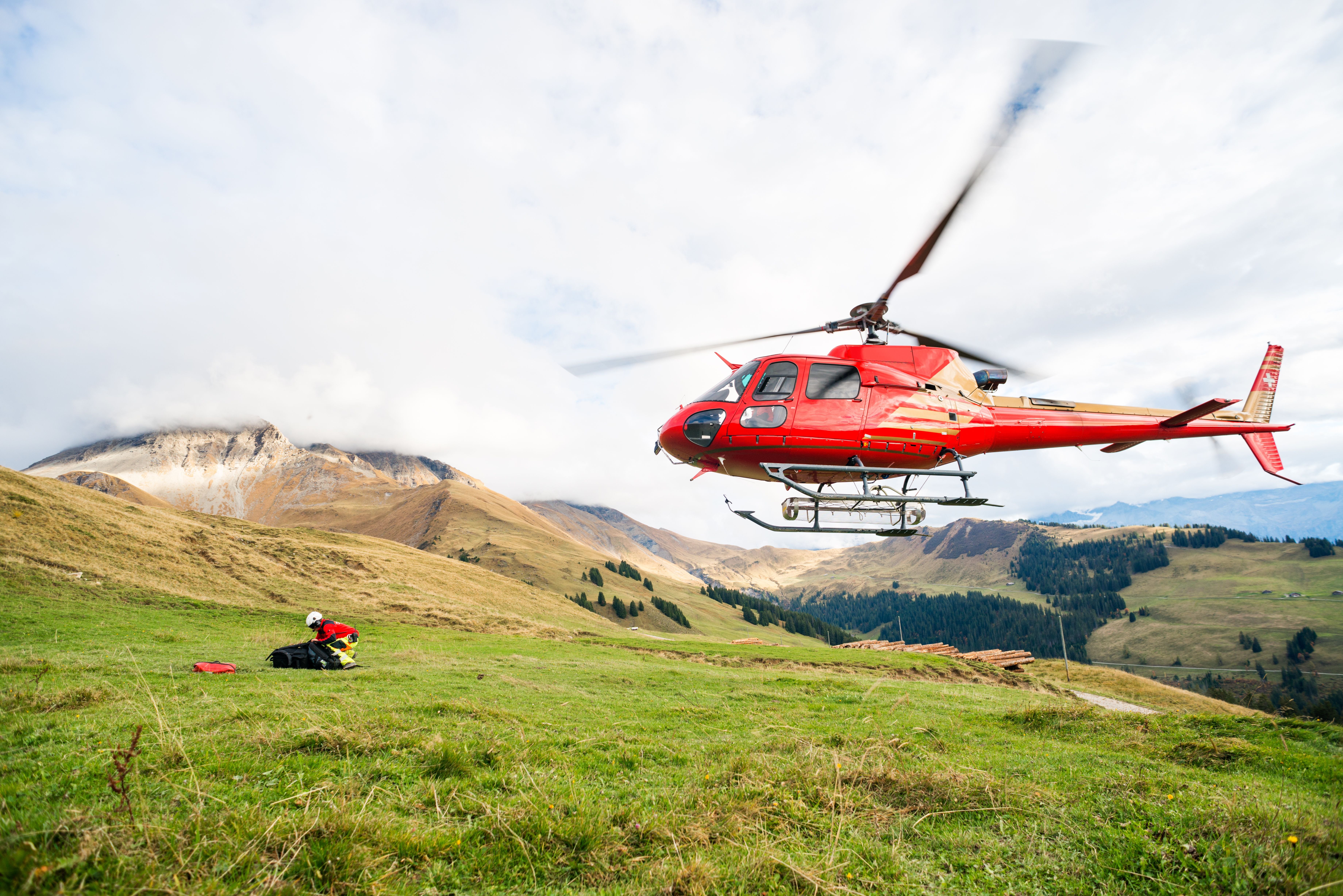 Roter Rettungshubschrauber startet auf einer grünen Bergwiese in den Schweizer Alpen.