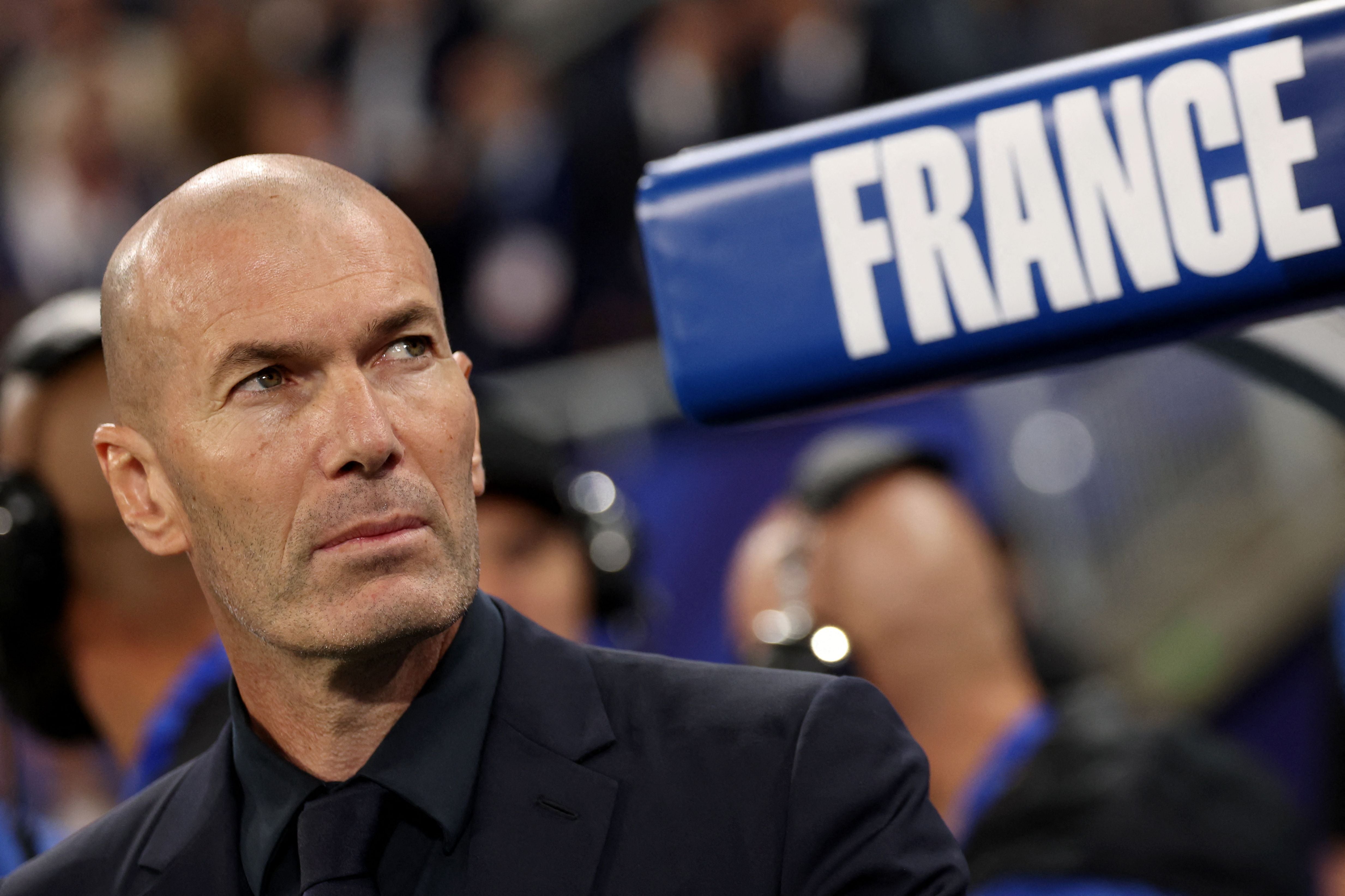 Ein Mann im Anzug blickt ernst, daneben ein Schild mit der Aufschrift "FRANCE".