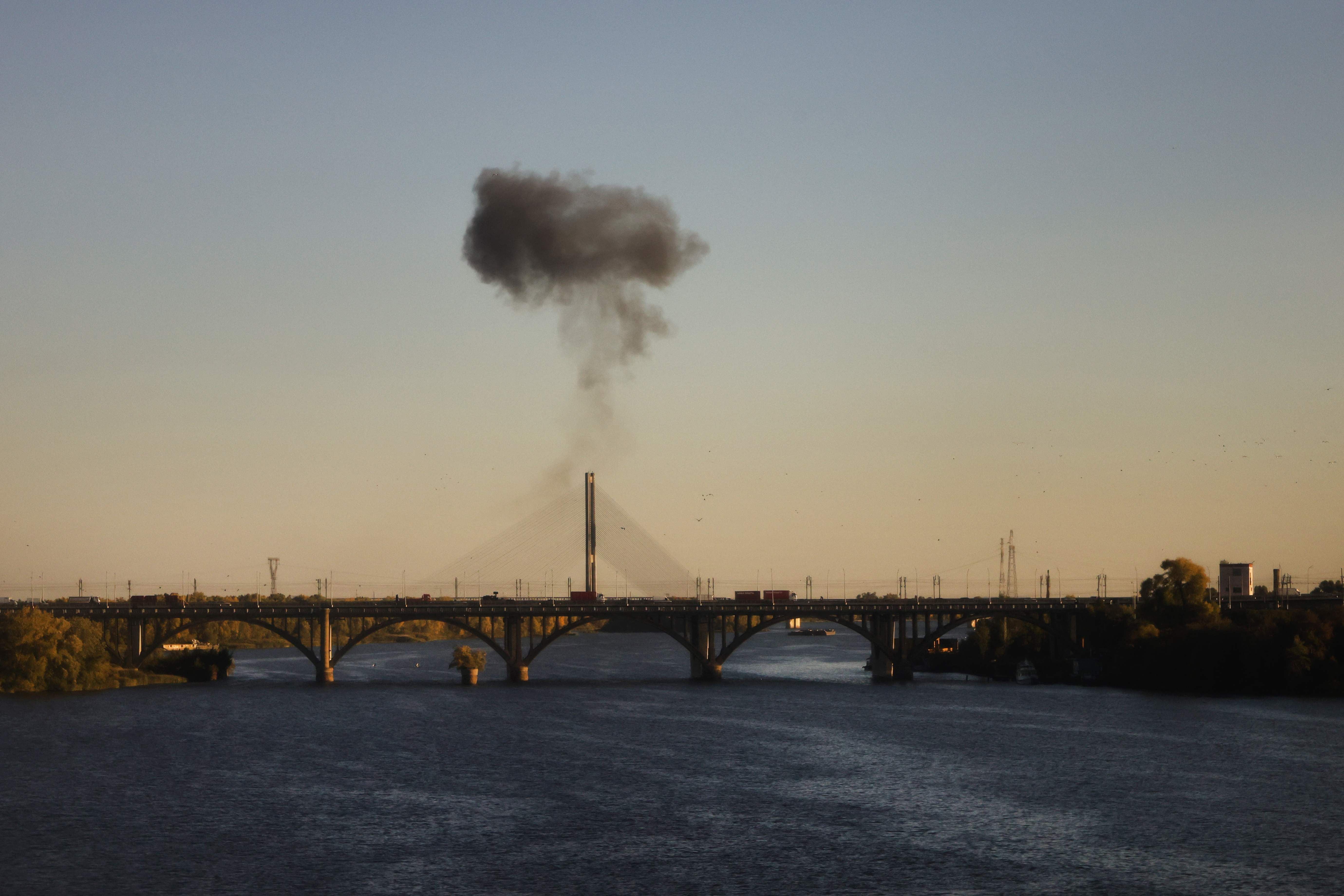 Schwarze Rauchwolke steigt über einer Brücke am Dnipro-Fluss bei Sonnenuntergang auf.