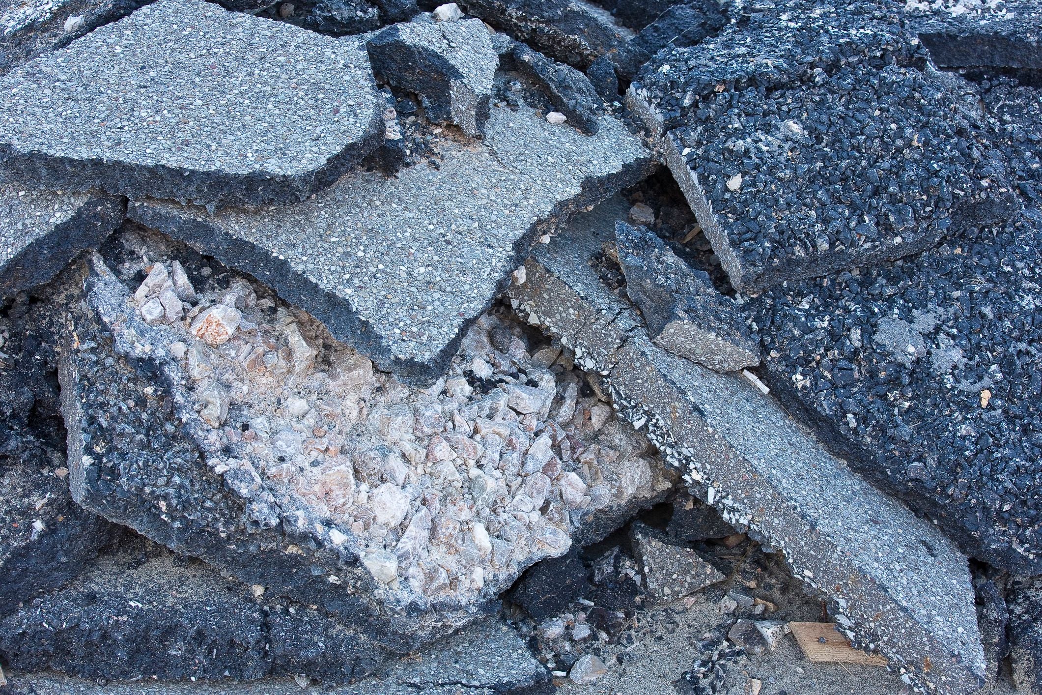 Gebrochene Asphaltschollen liegen übereinander nach Straßenabriss auf einer Baustelle.