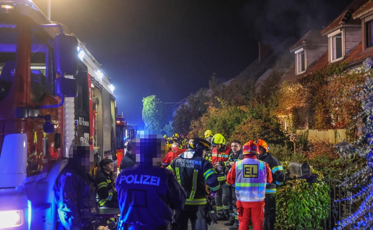 Feuerwehr und Polizei im Einsatz vor einem rauchenden Wohnhaus in der Nacht.