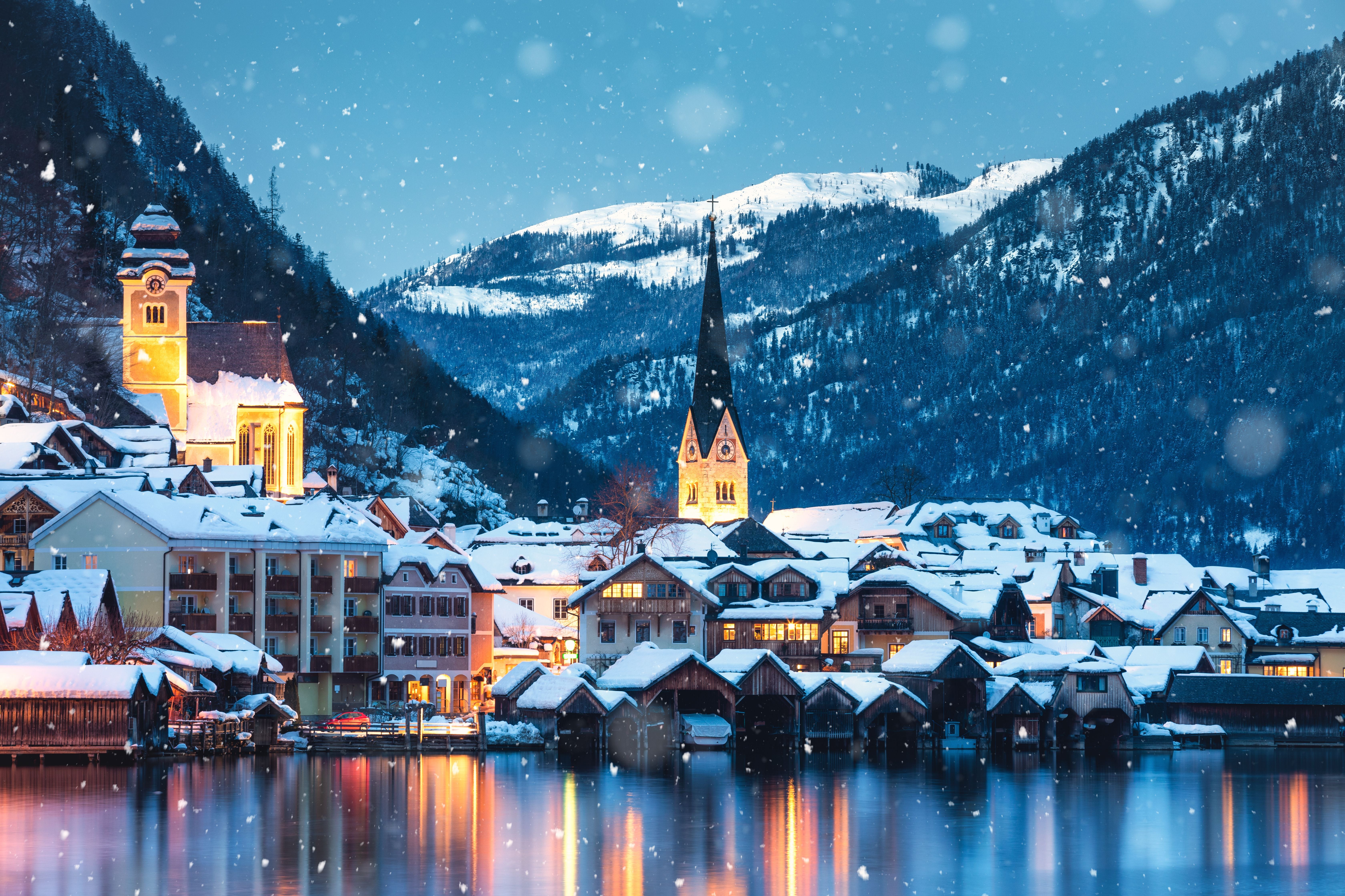 Verschneite Häuser und beleuchtete Kirche am See im winterlichen Hallstatt, Österreich.