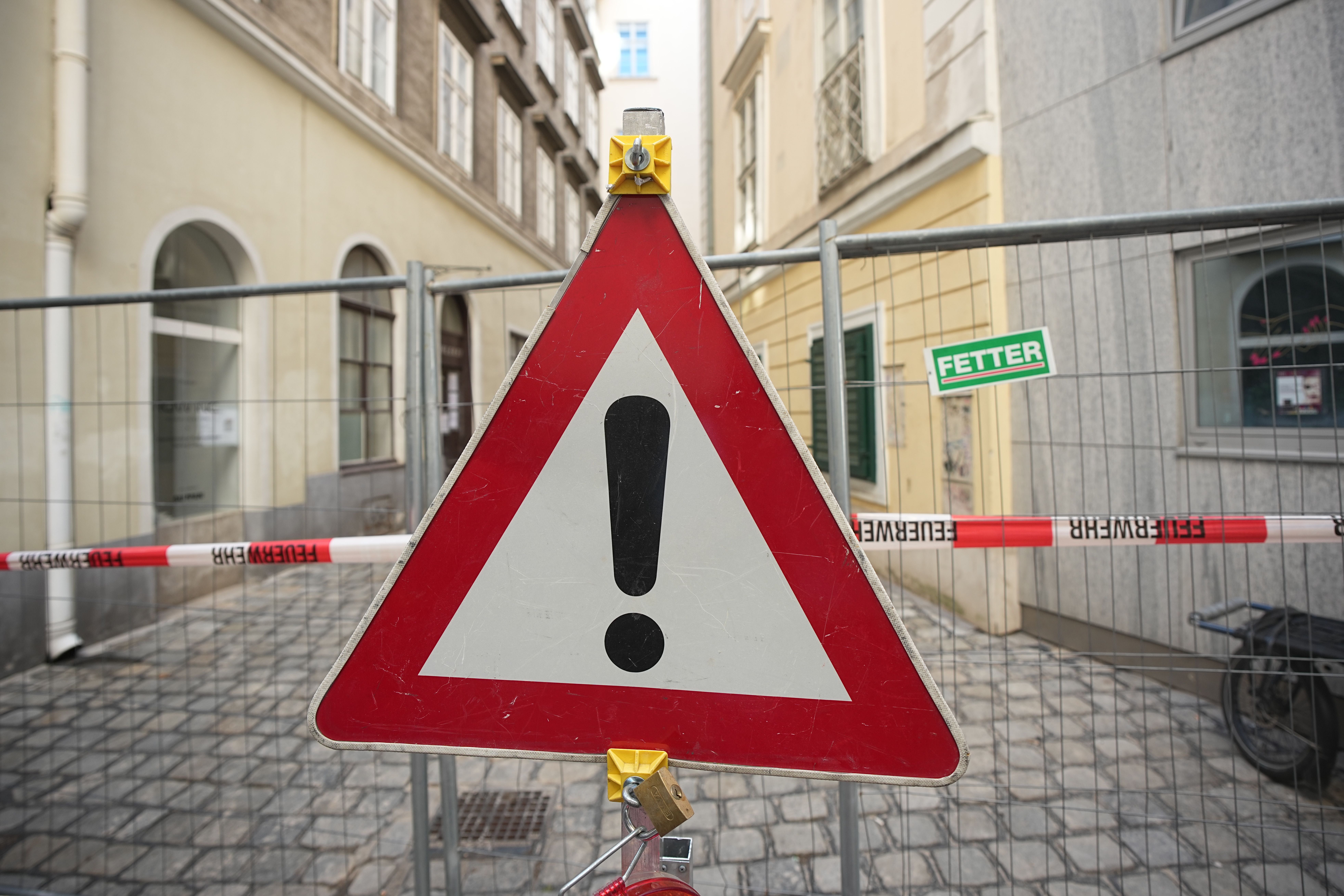 Warnschild mit Ausrufezeichen vor einer abgesperrten Gasse in einer Innenstadt.