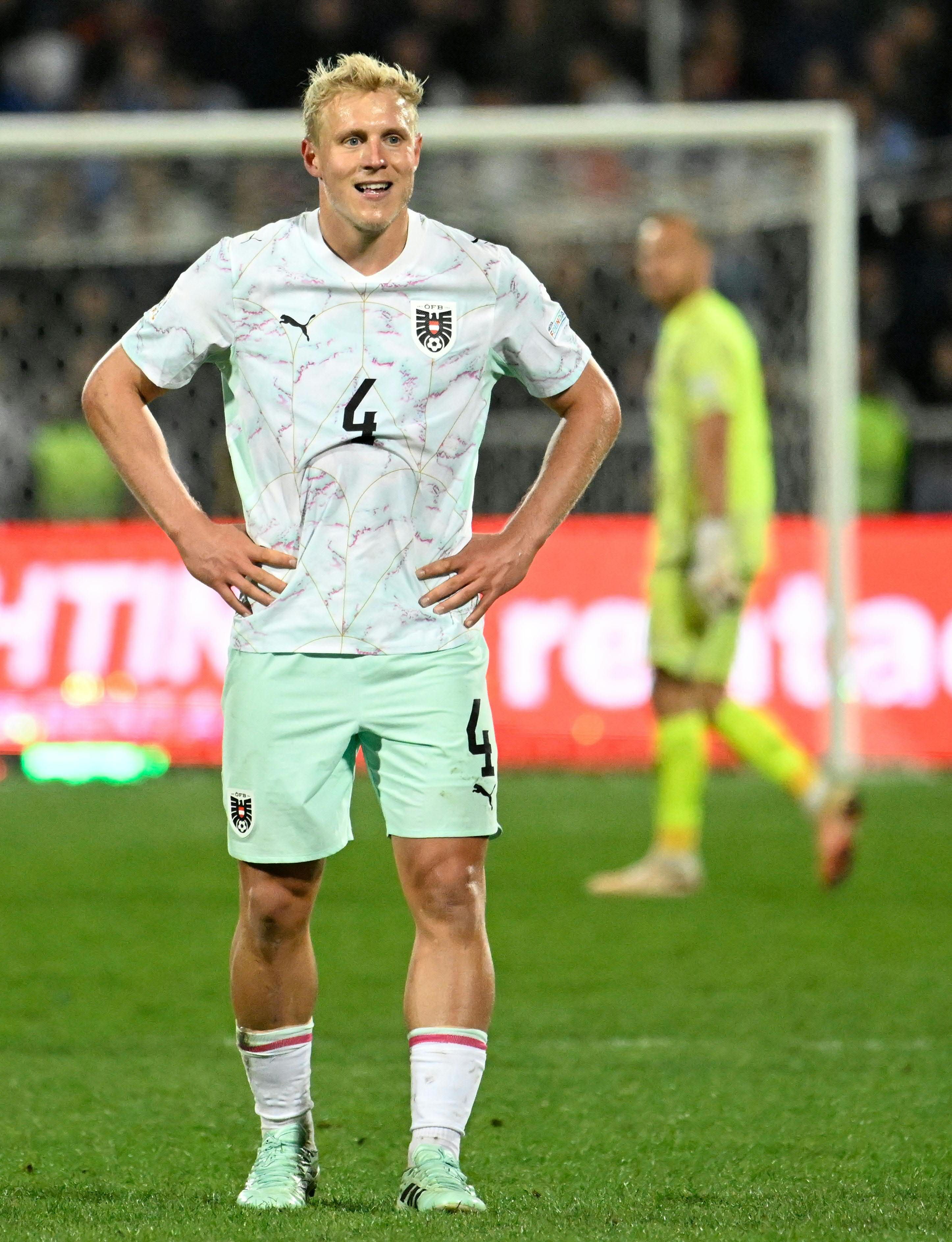 Xaver Schlager steht im weiß-hellgrünen Nationalteam-Trikot mit der Rückennummer 4 und den Händen an den Hüften auf dem Fußballplatz.