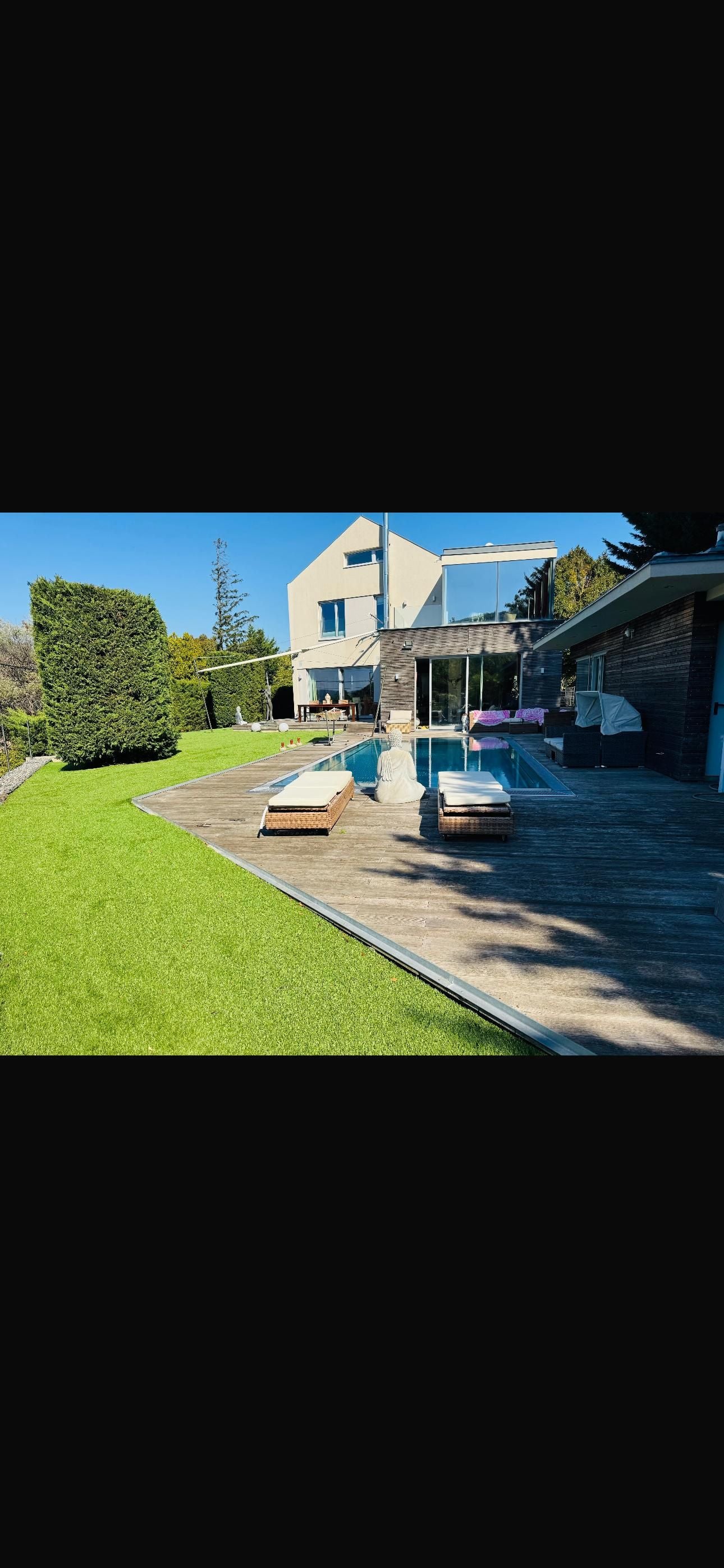 Mausis Terrasse mit Liegestühlen, Pool und gepflegtem Rasen vor einem Haus an einem sonnigen Tag.