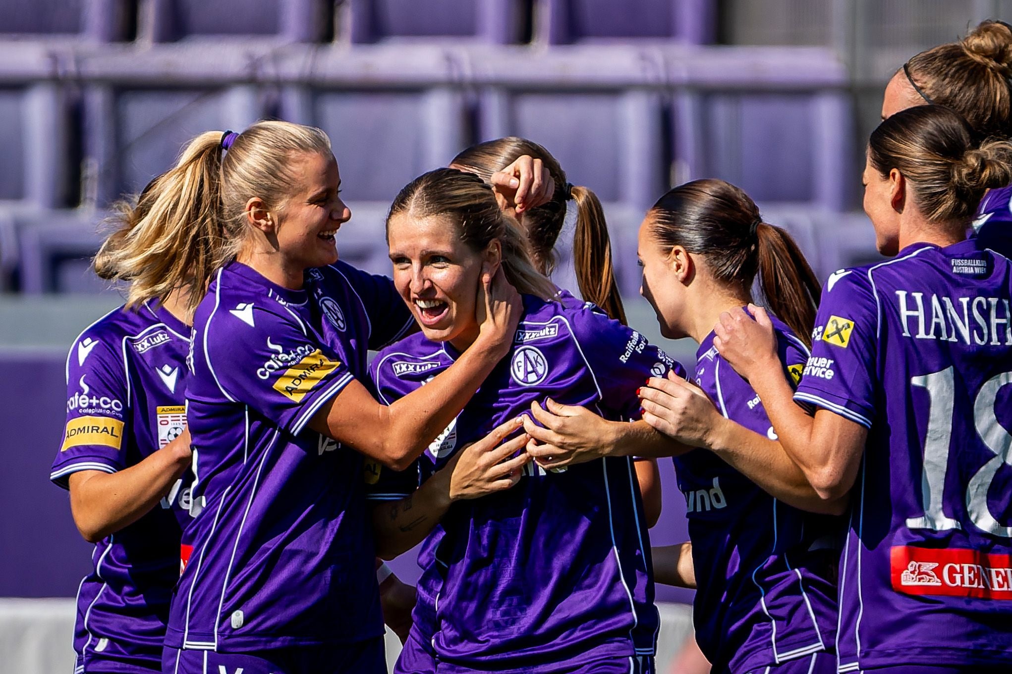 Mehrere Fußballspielerinnen in violetten Trikots jubeln gemeinsam nach einem Tor.