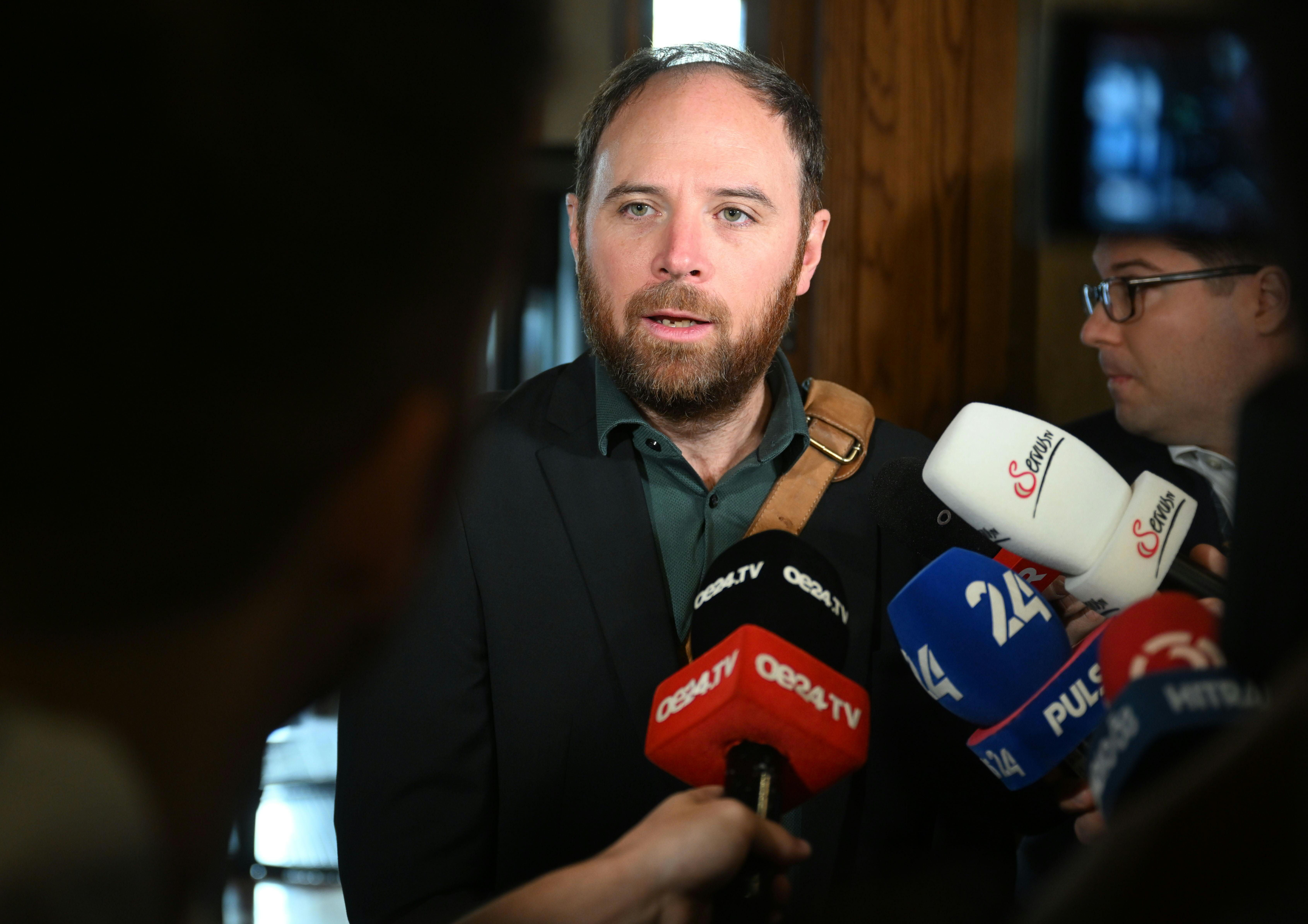Ein Mann spricht vor mehreren Mikrofonen auf einer Pressekonferenz in einem Gebäude.