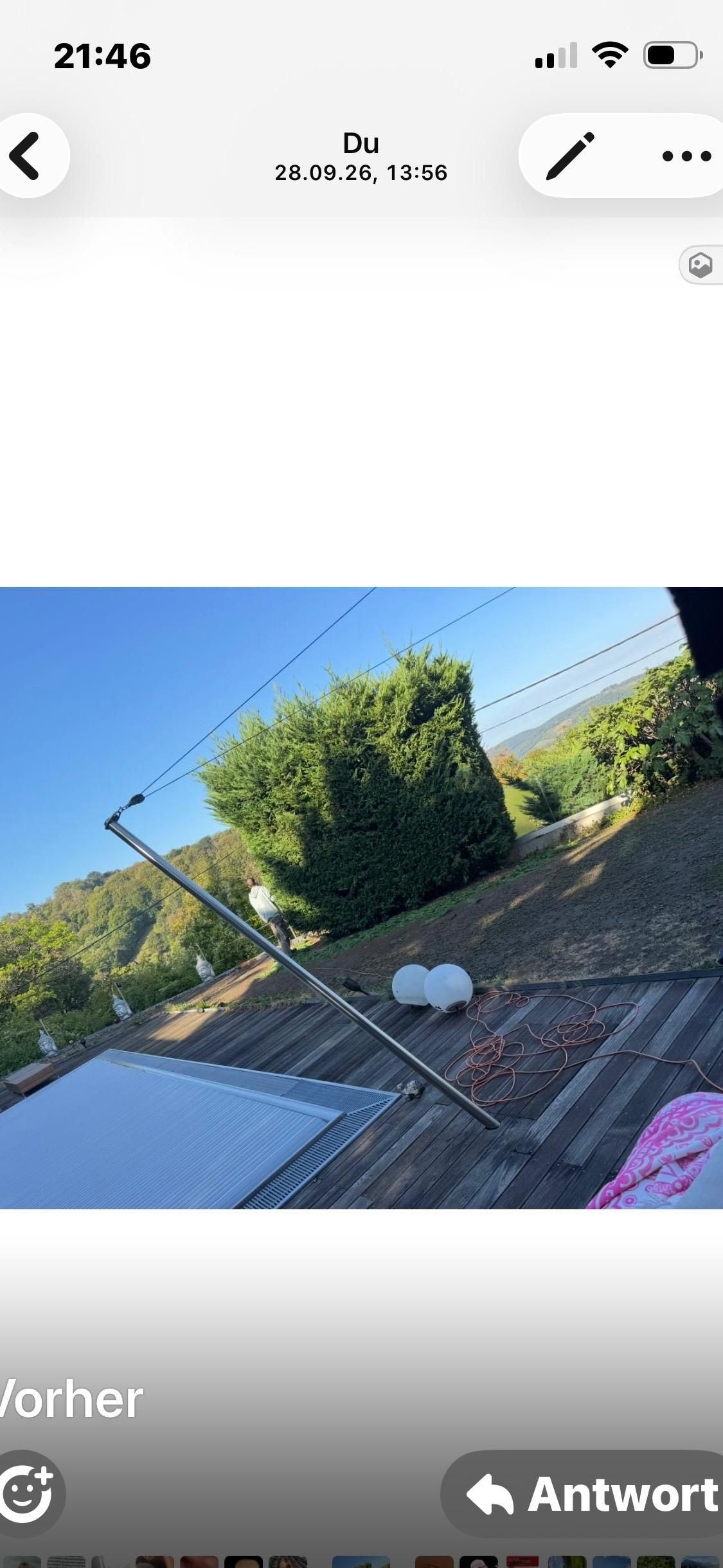 Holzterrasse mit Pool, Büschen, Gartenblick und leuchtenden Kugeln bei sonnigem Wetter.