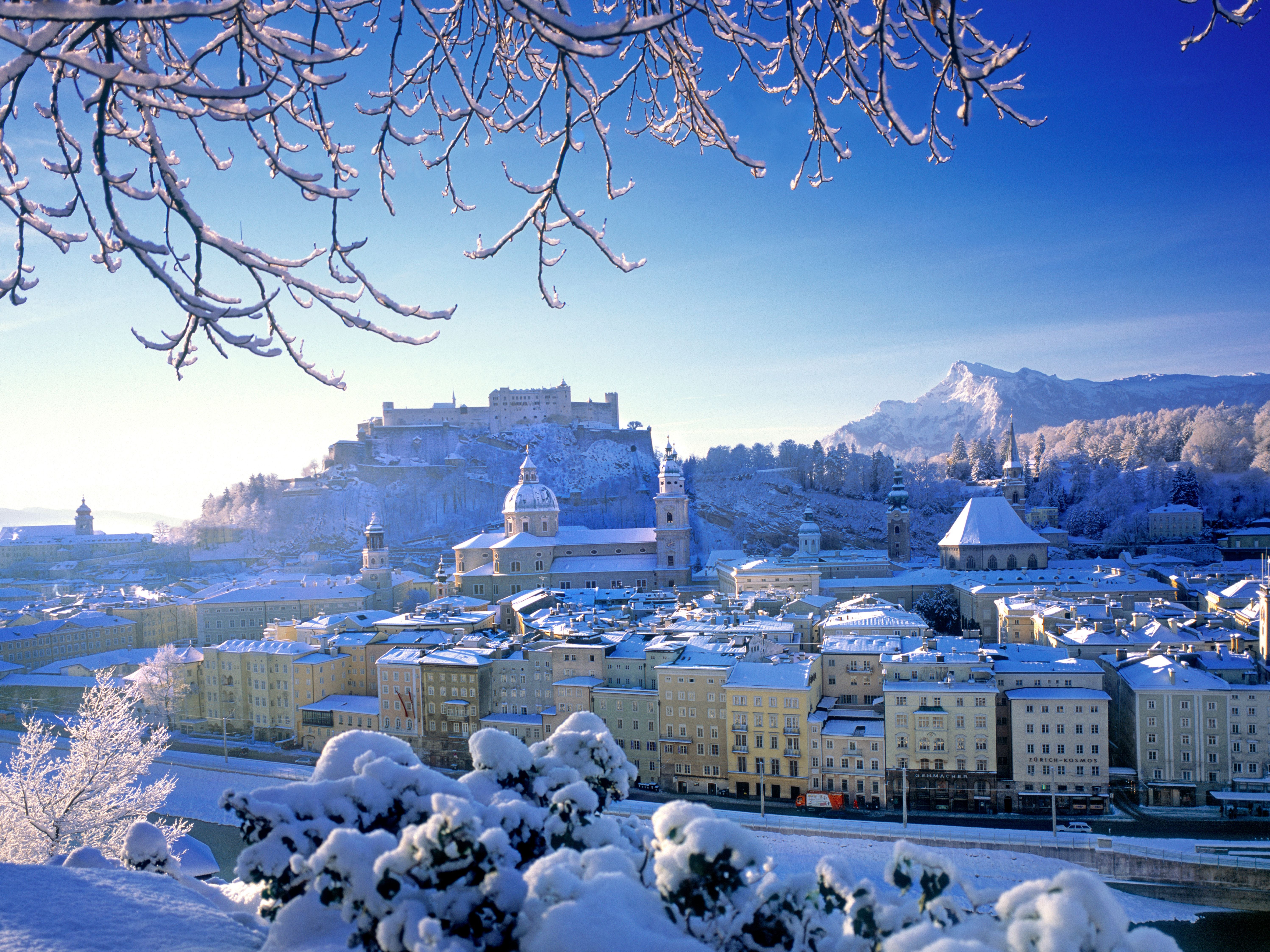 Blick auf eine verschneite Stadt mit historischen Gebäuden und Bergen im Hintergrund.