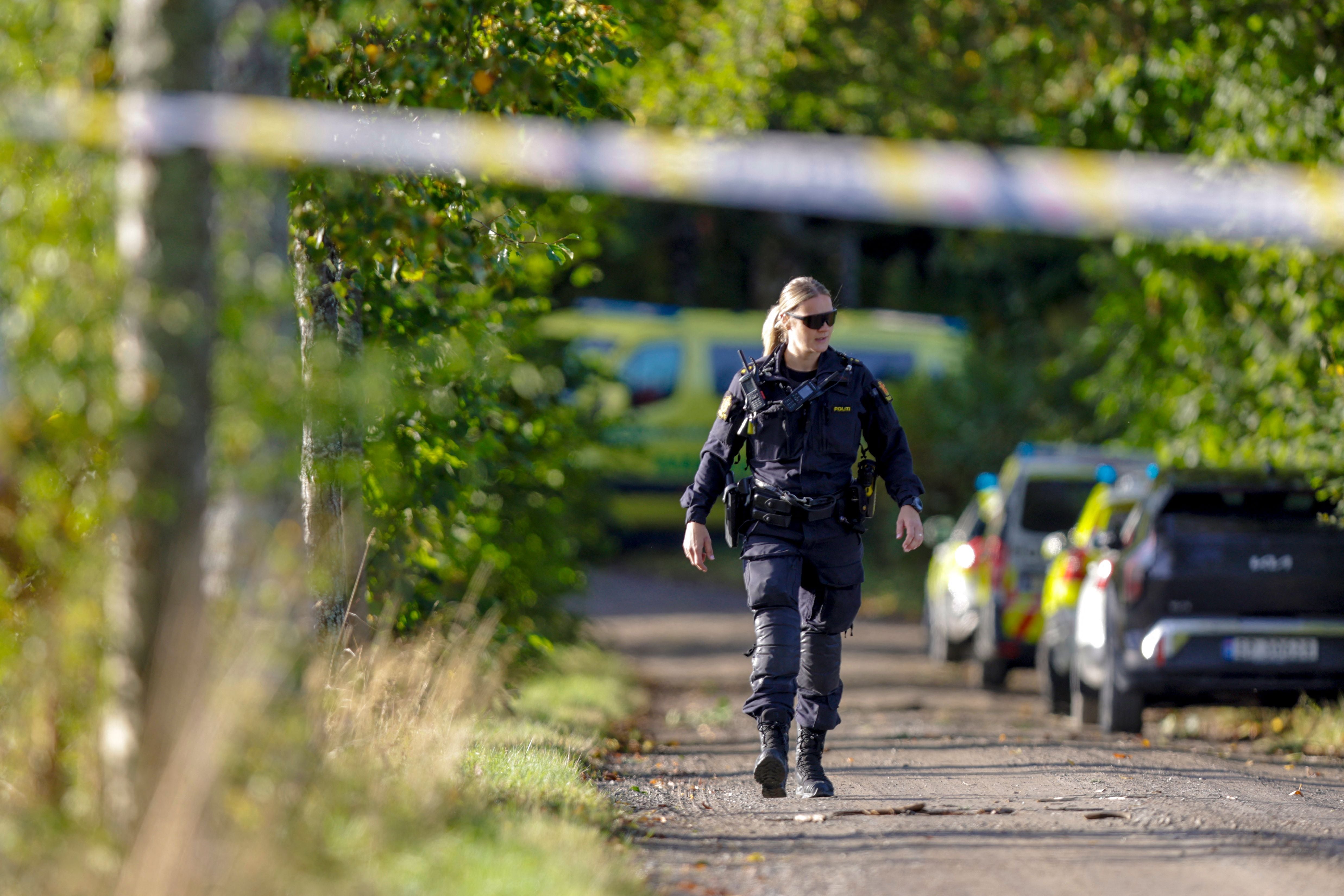 Eine Polizistin geht auf einer abgesperrten Straße mit Einsatzfahrzeugen im Hintergrund.