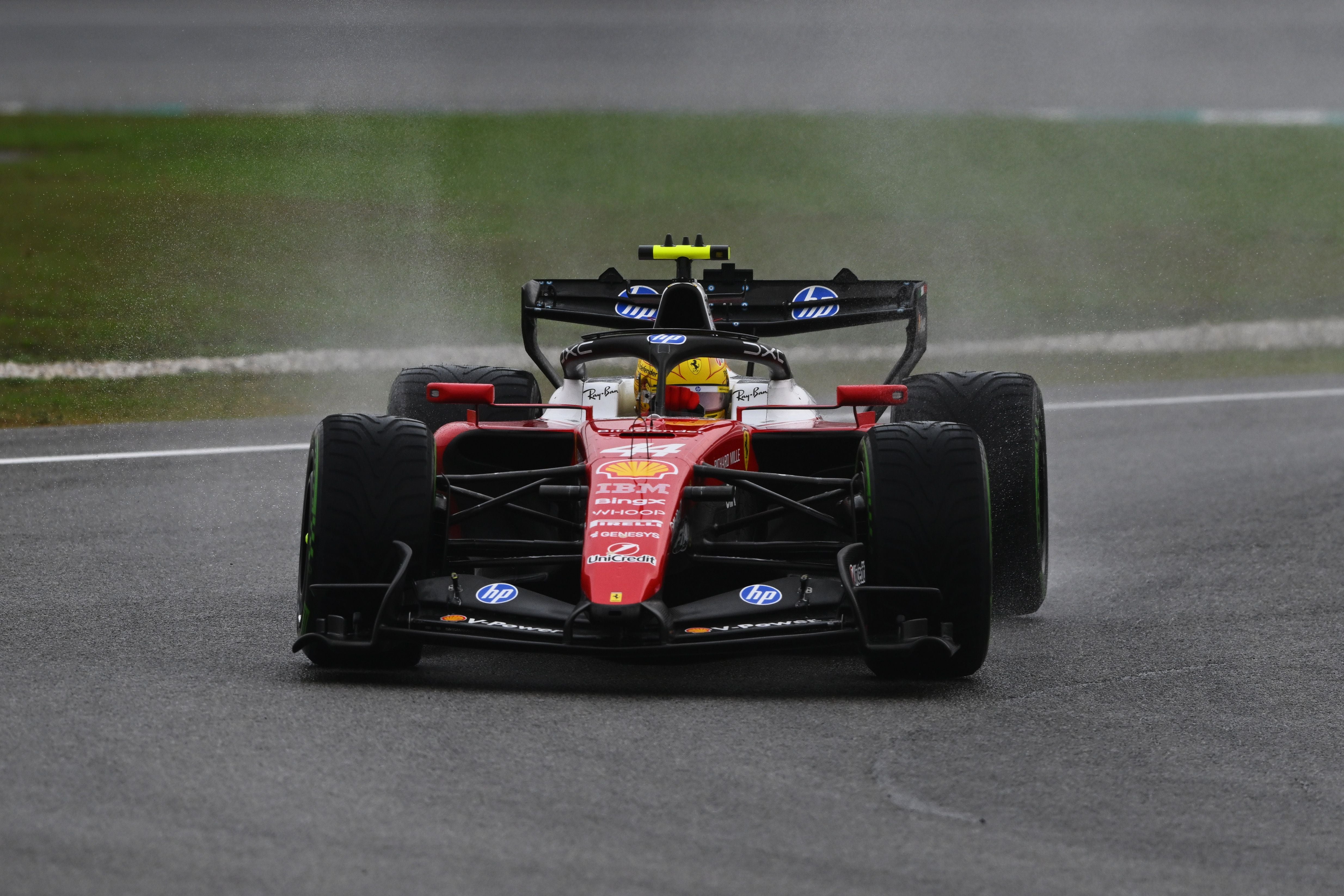 Ein roter Formel-1-Wagen fährt bei nasser Strecke auf einer Rennstrecke.