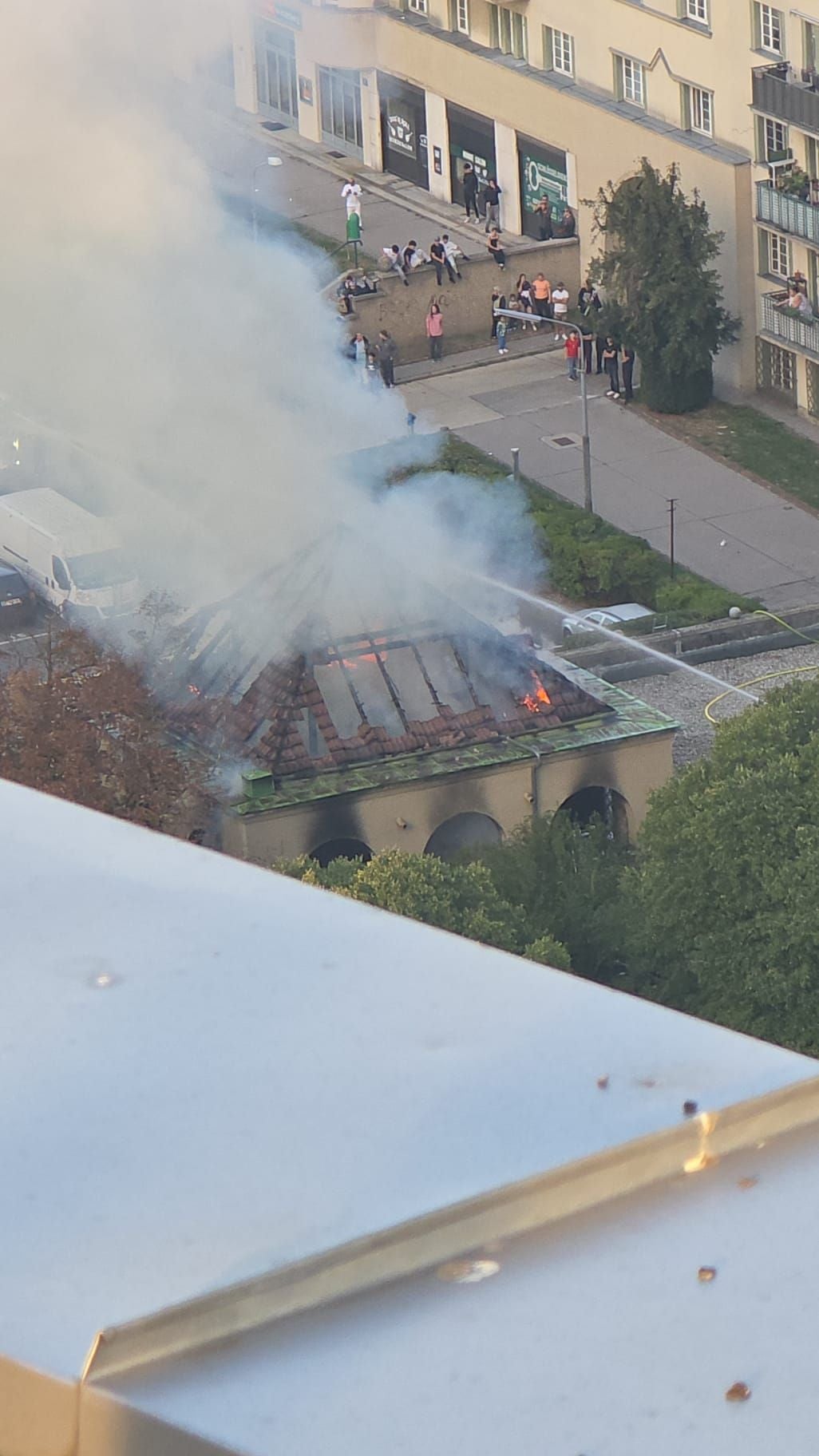 Dach eines Gebäudes im Fliederhof brennt, starker Rauch steigt auf, Menschen beobachten.