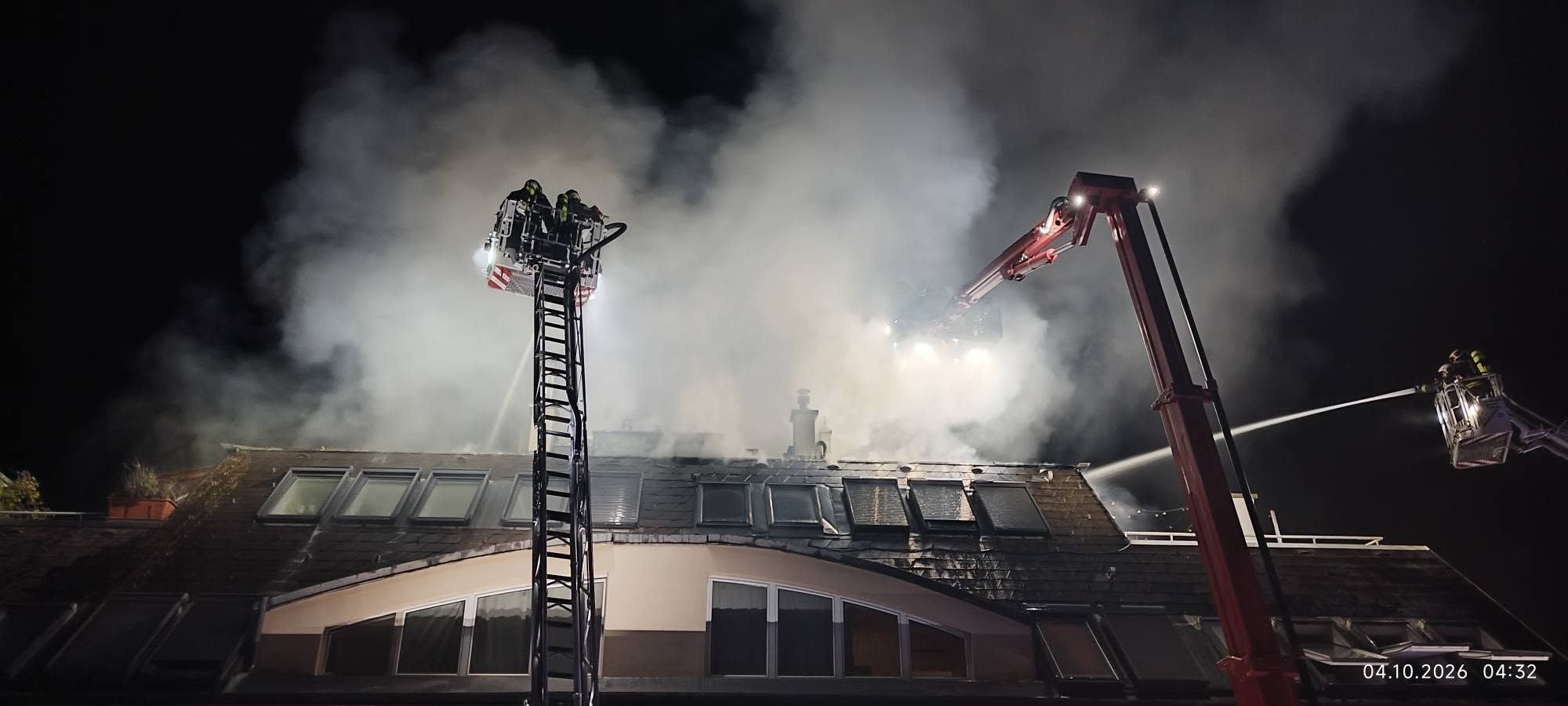 Feuerwehr bekämpft nachts Brand auf dem Dach eines Gebäudes mit Drehleitern und Wasserstrahlen.