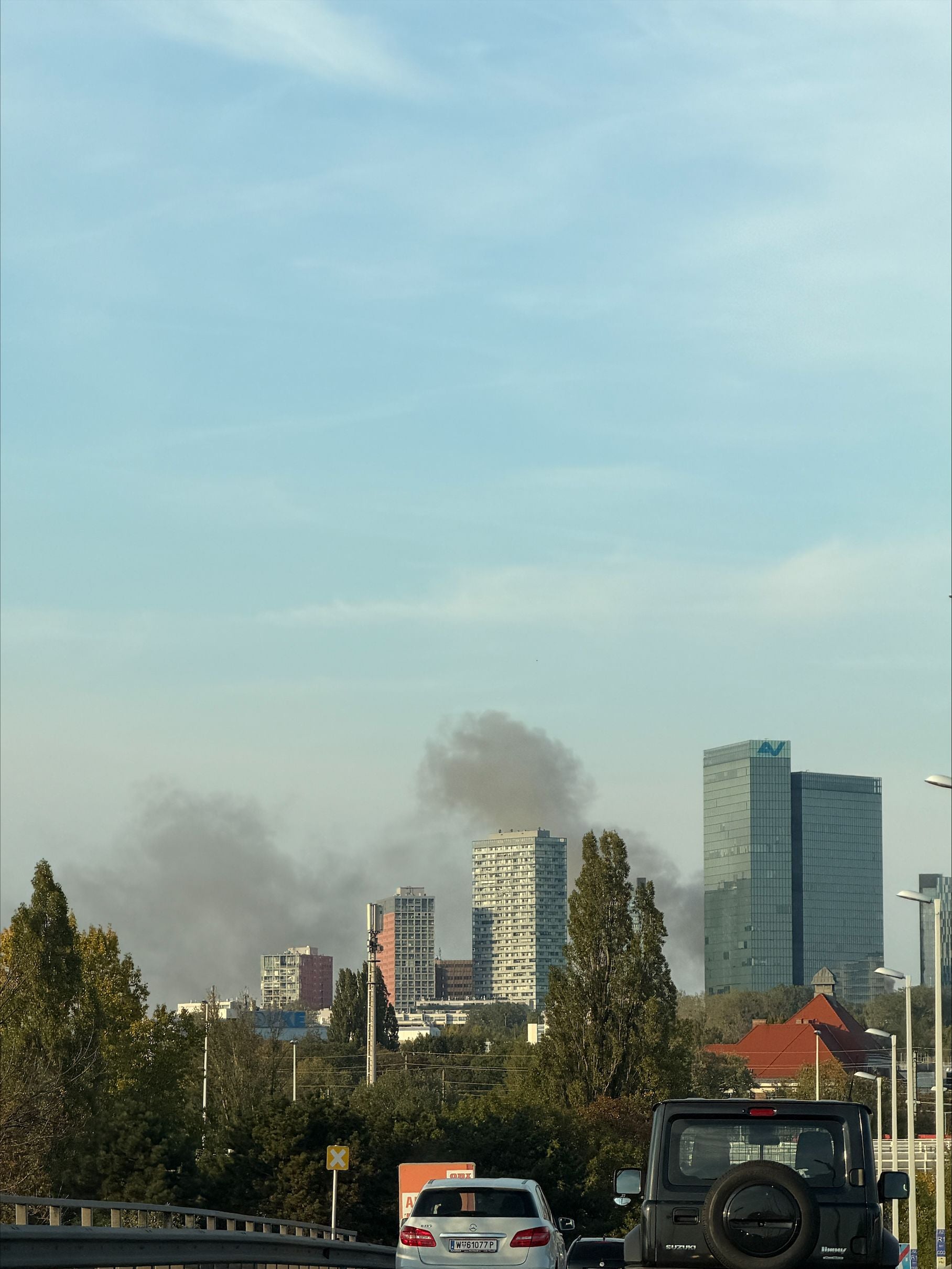 Schwarzer Rauch steigt hinter Hochhäusern im 10. Bezirk auf, Autos stehen im Vordergrund.