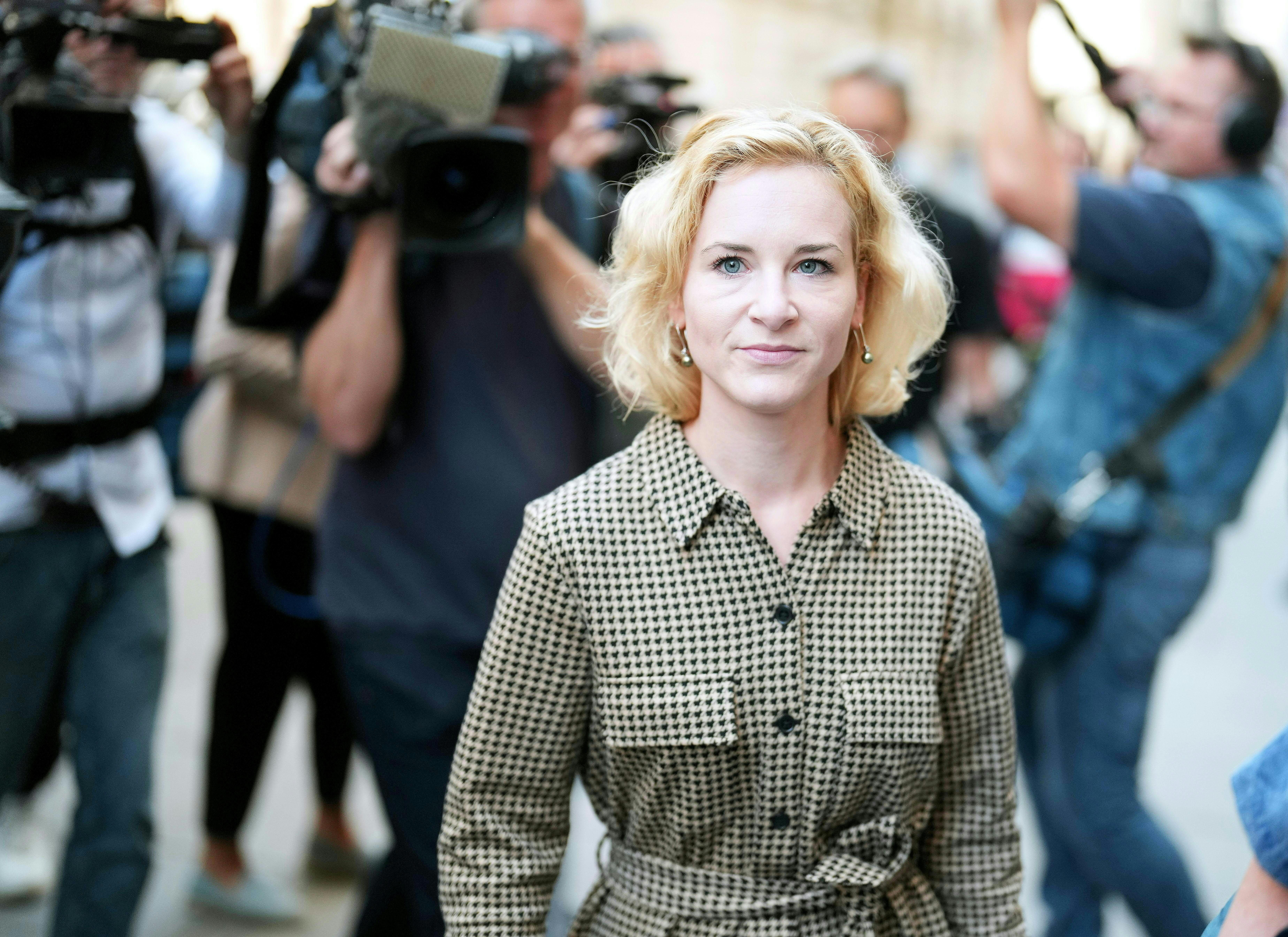 Eine Frau steht im Vordergrund, hinter ihr Kameraleute und Fotografen bei einer Veranstaltung.