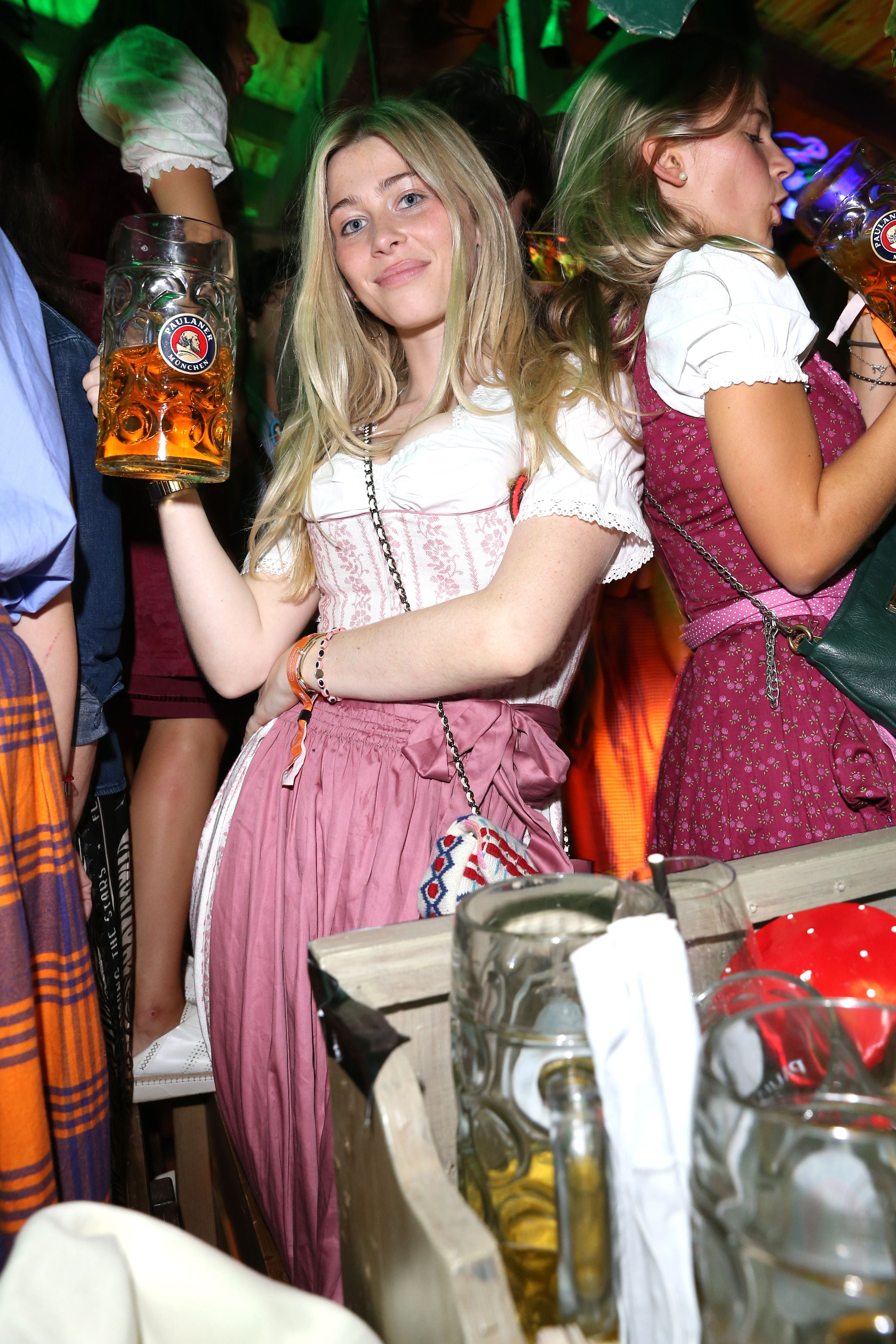 Junge Frau im Dirndl hält einen Bierkrug auf dem Oktoberfest, umgeben von feiernden Menschen.