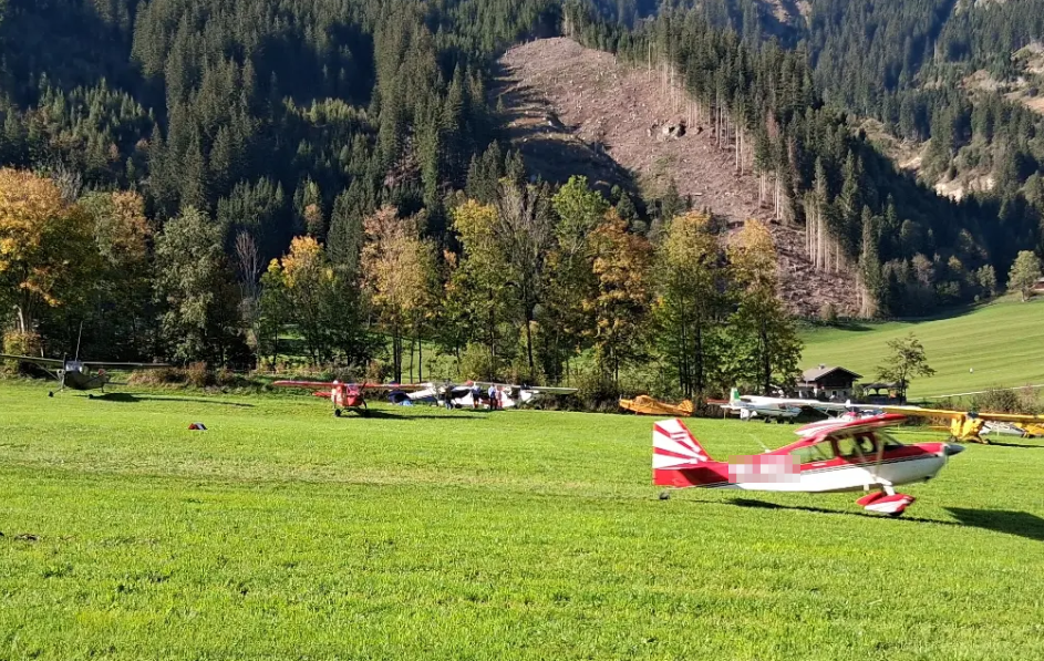 Kleine Sportflugzeuge stehen auf einer Wiese vor bewaldeten Bergen beim Fly-in in Krimml.