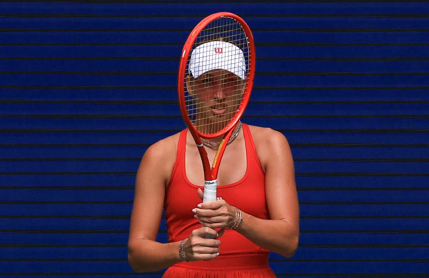 Tennisspielerin hält Schläger vor ihr Gesicht auf einem Tennisplatz mit blauem Hintergrund.