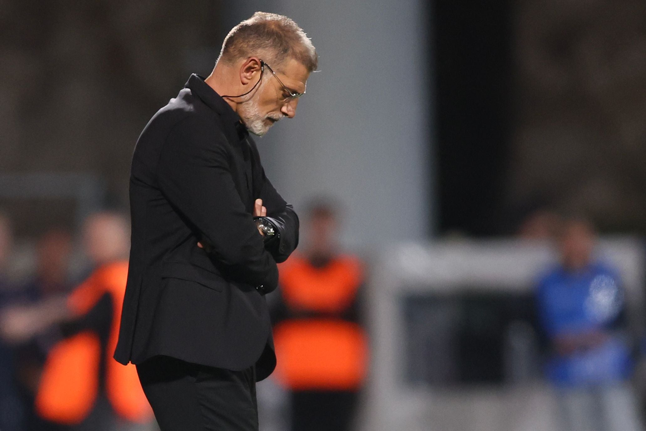 Ein Mann im Anzug steht mit verschränkten Armen und gesenktem Kopf am Spielfeldrand.