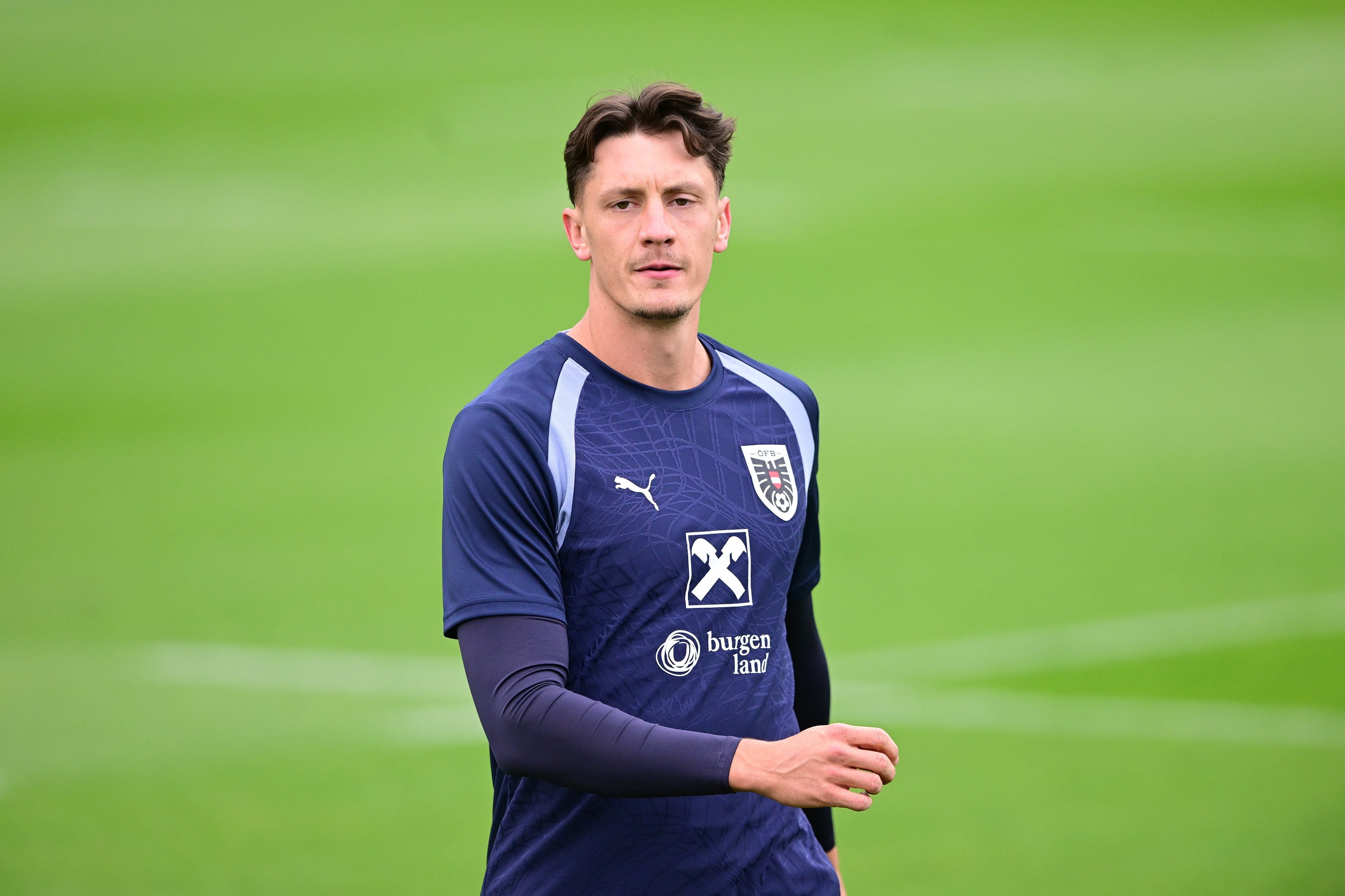 Ein Fußballspieler im Trainingsanzug steht auf einem grünen Rasenplatz.